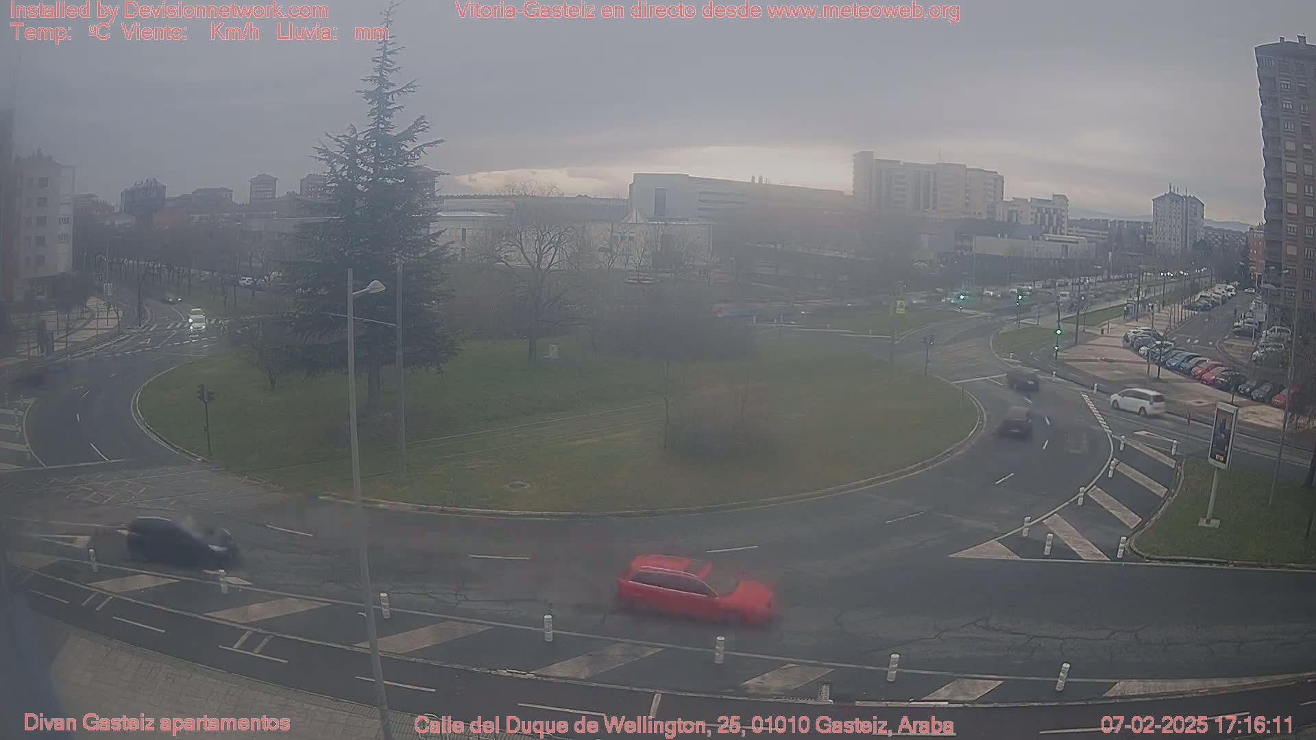 A hazy, overcast day reveals a roundabout in a city with several cars and buildings in the background.