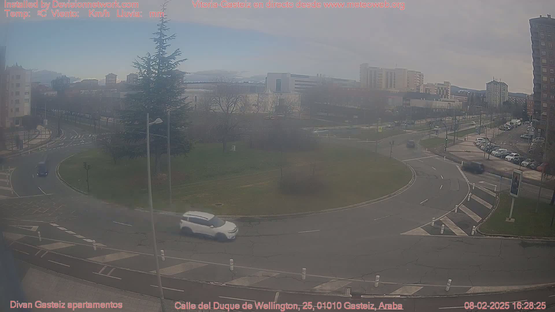 A hazy view of a roundabout in a city, with several cars visible and buildings in the background.