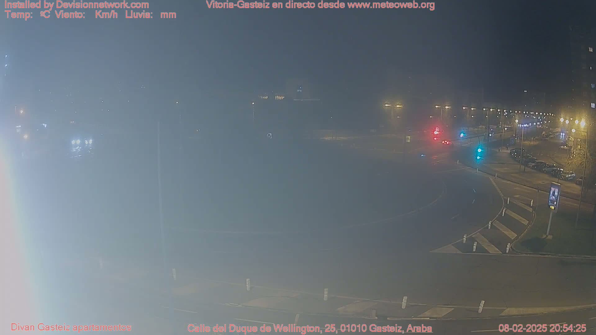 A foggy nighttime view of a roundabout intersection with sparse traffic and streetlights.