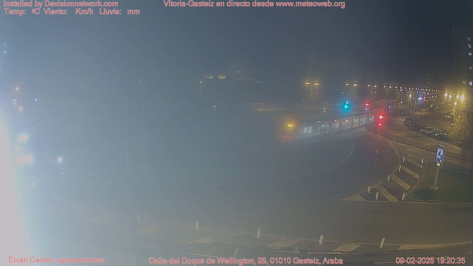 A foggy nighttime street intersection shows a few cars and a streetlight.