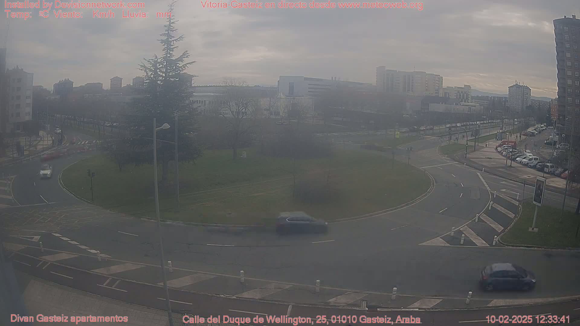A hazy view of a roundabout in a city with several cars and buildings visible in the background.