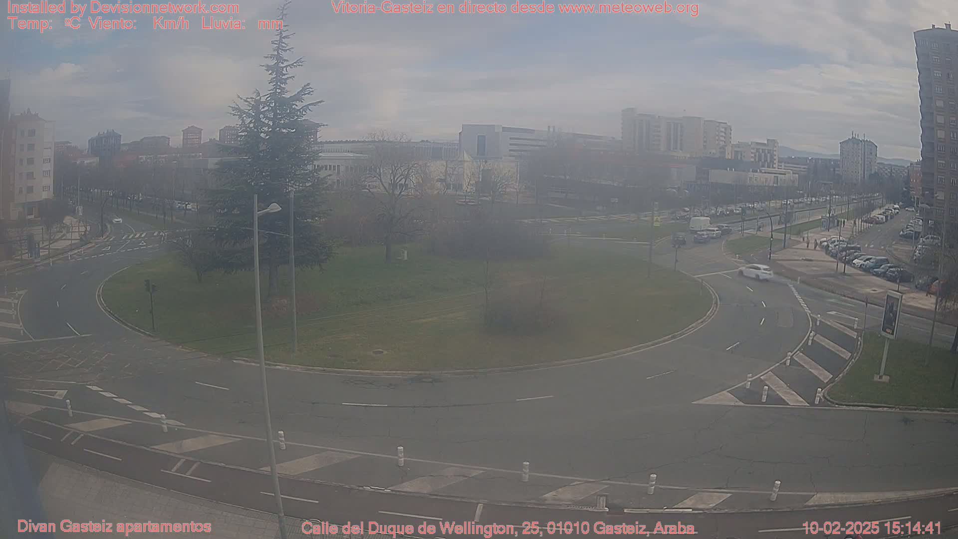 A hazy view of a roundabout in a city, with several cars visible and buildings in the background.