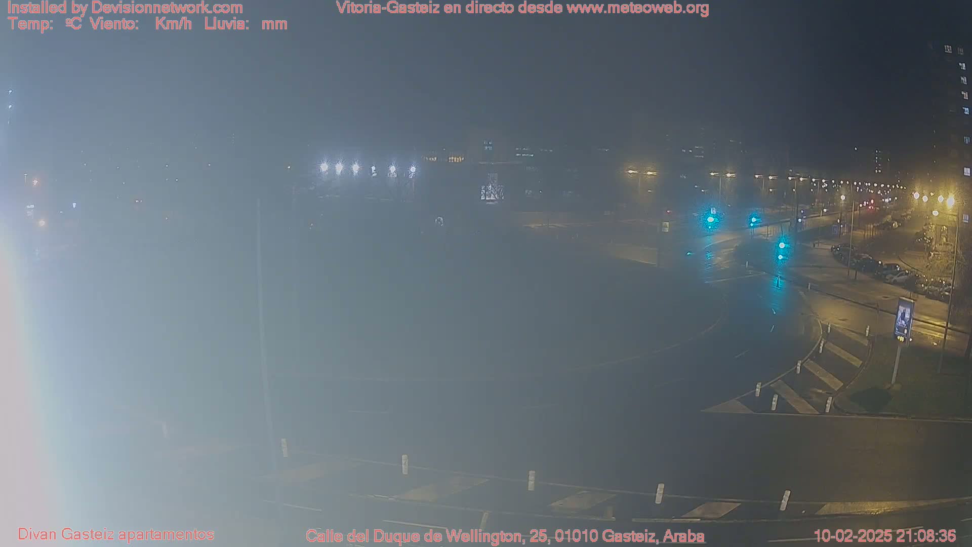 A nighttime, wet road intersection with several cars and streetlights.