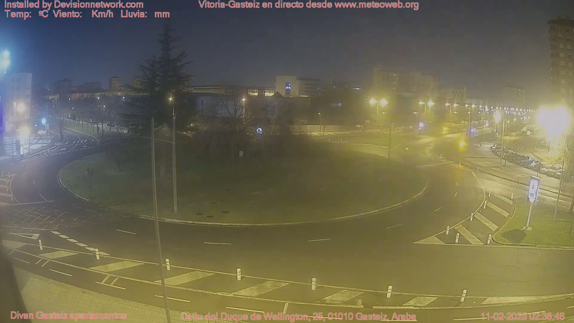A nighttime view of a roundabout in a city, with cars visible and streetlights illuminating the scene.