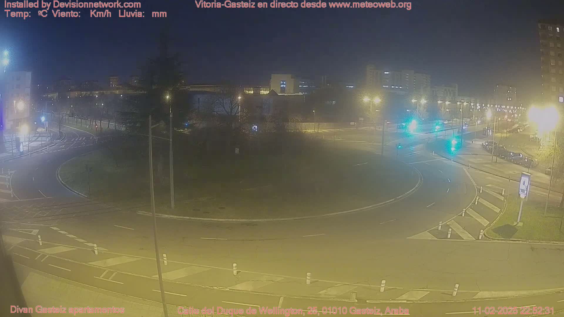 A nighttime view of a roundabout in a city with several cars and streetlights visible.