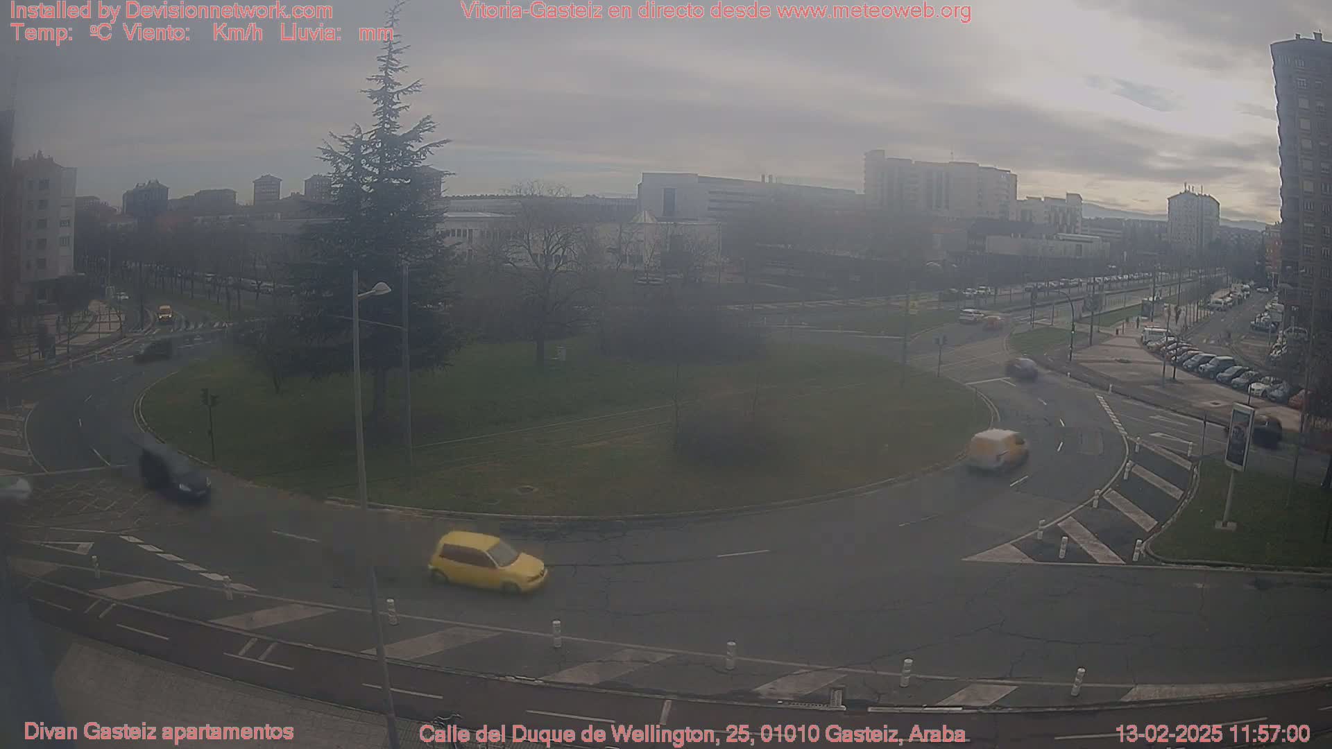 A hazy, overcast day shows a traffic circle with several cars, surrounded by buildings and trees.