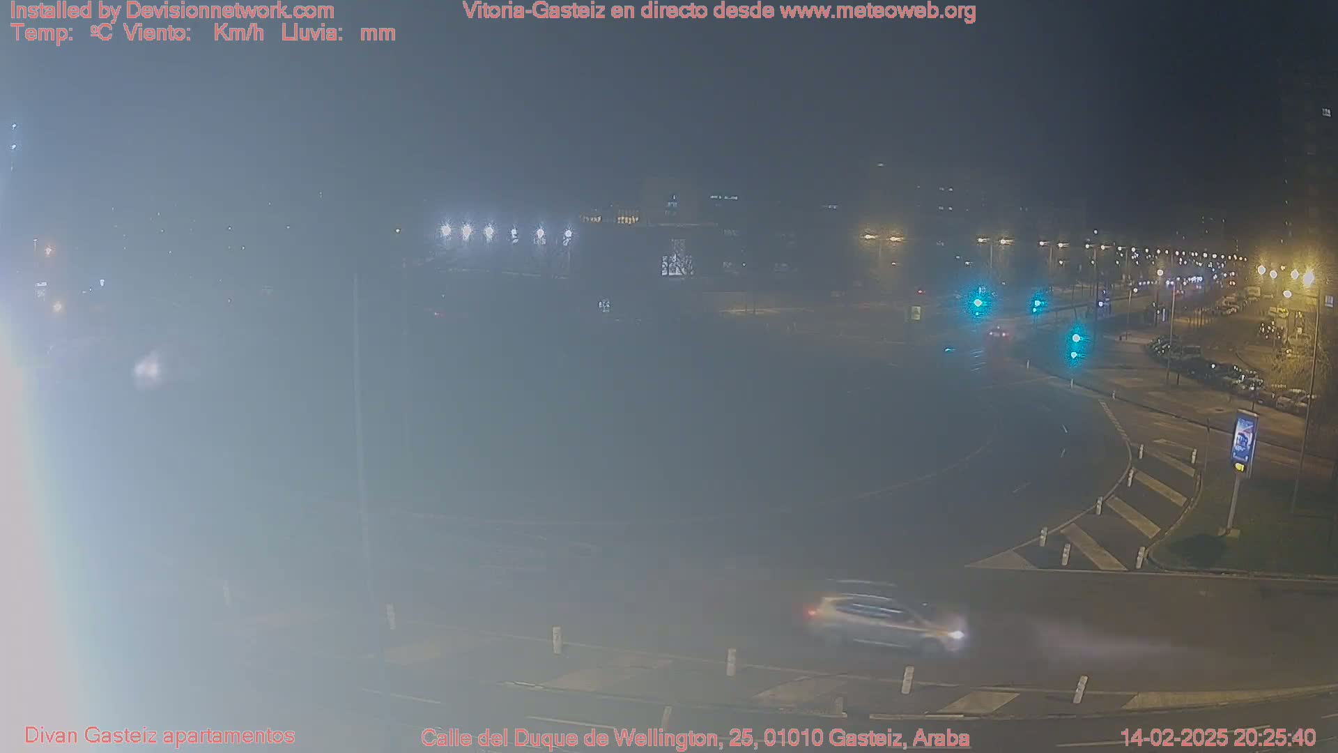 A foggy night scene shows a roundabout with a few cars and streetlights illuminating the area.