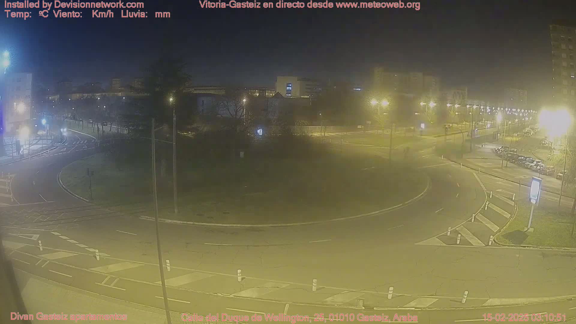 A nighttime view of a roundabout with cars and streetlights, under hazy conditions.
