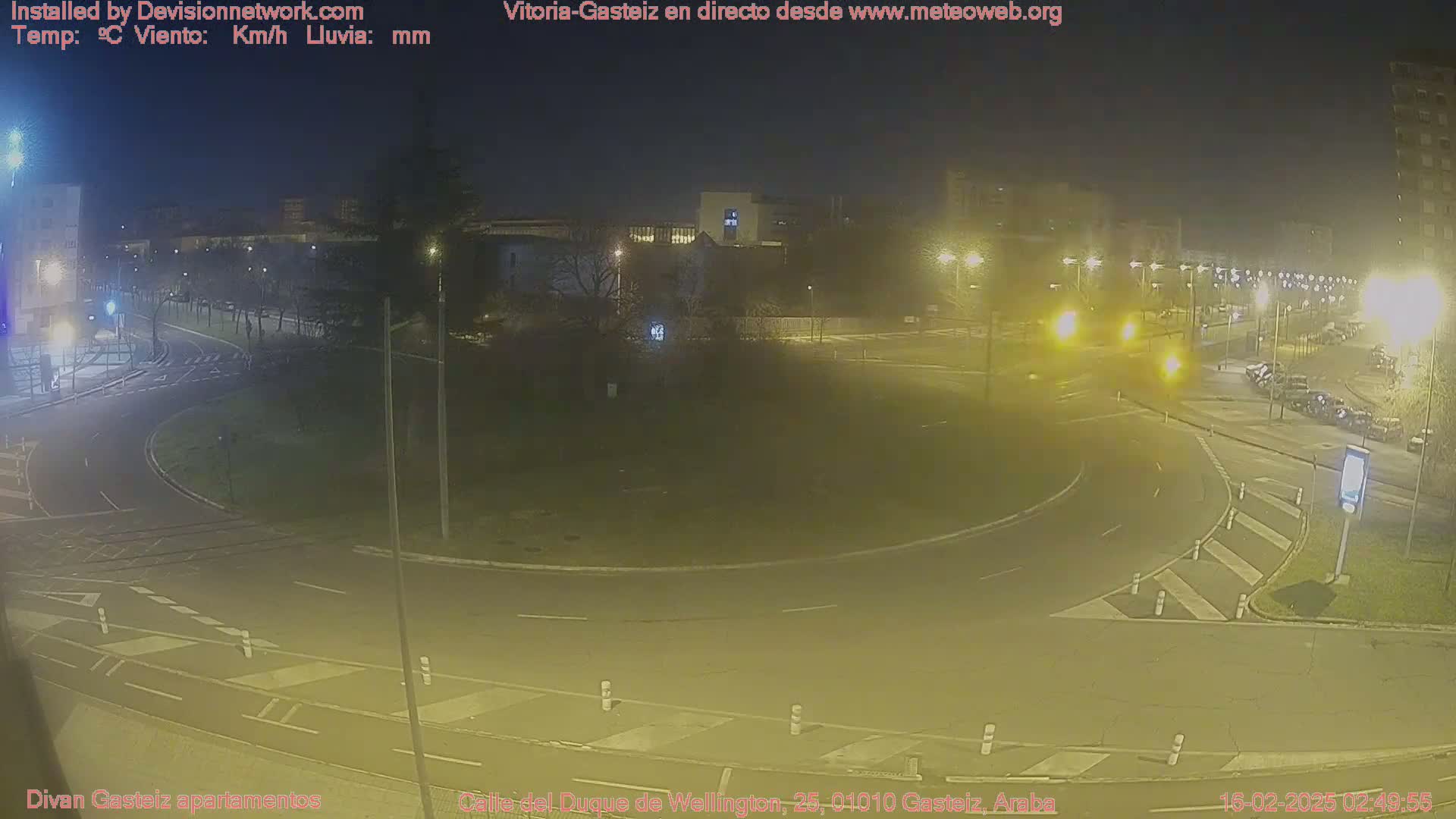 A nighttime view of a roundabout with cars and buildings in the background under artificial light.