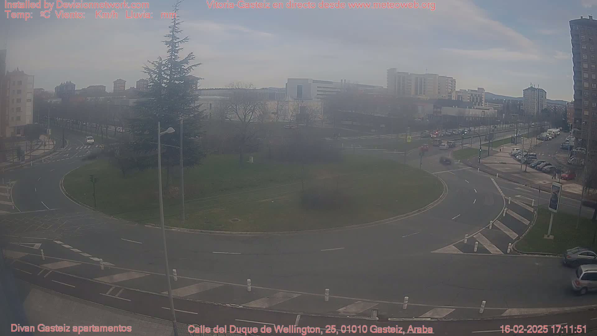 A hazy view of a roundabout with light traffic in a city, under a mostly cloudy sky.