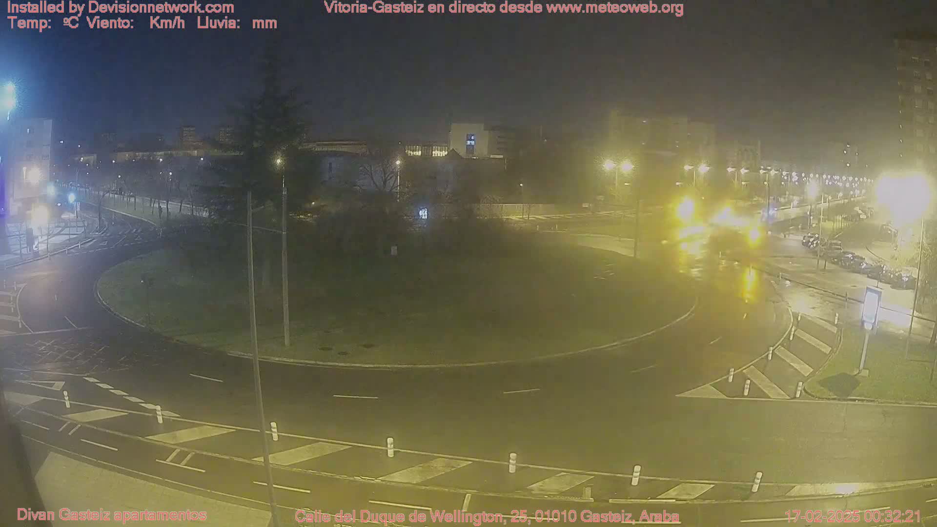 A wet, nighttime view of a roundabout with cars and streetlights.