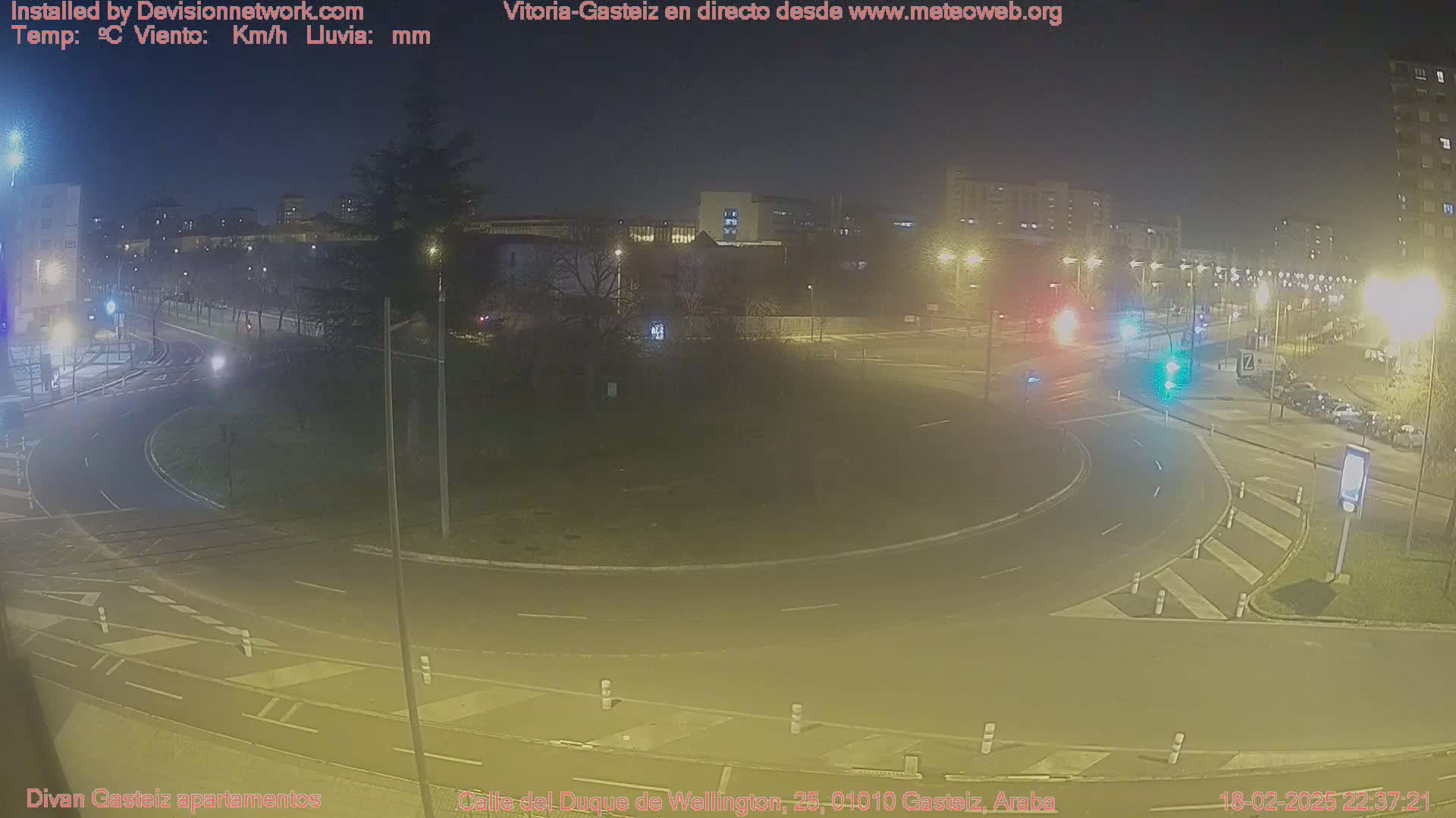A nighttime view of a roundabout with sparse traffic and streetlights illuminating a city streetscape.