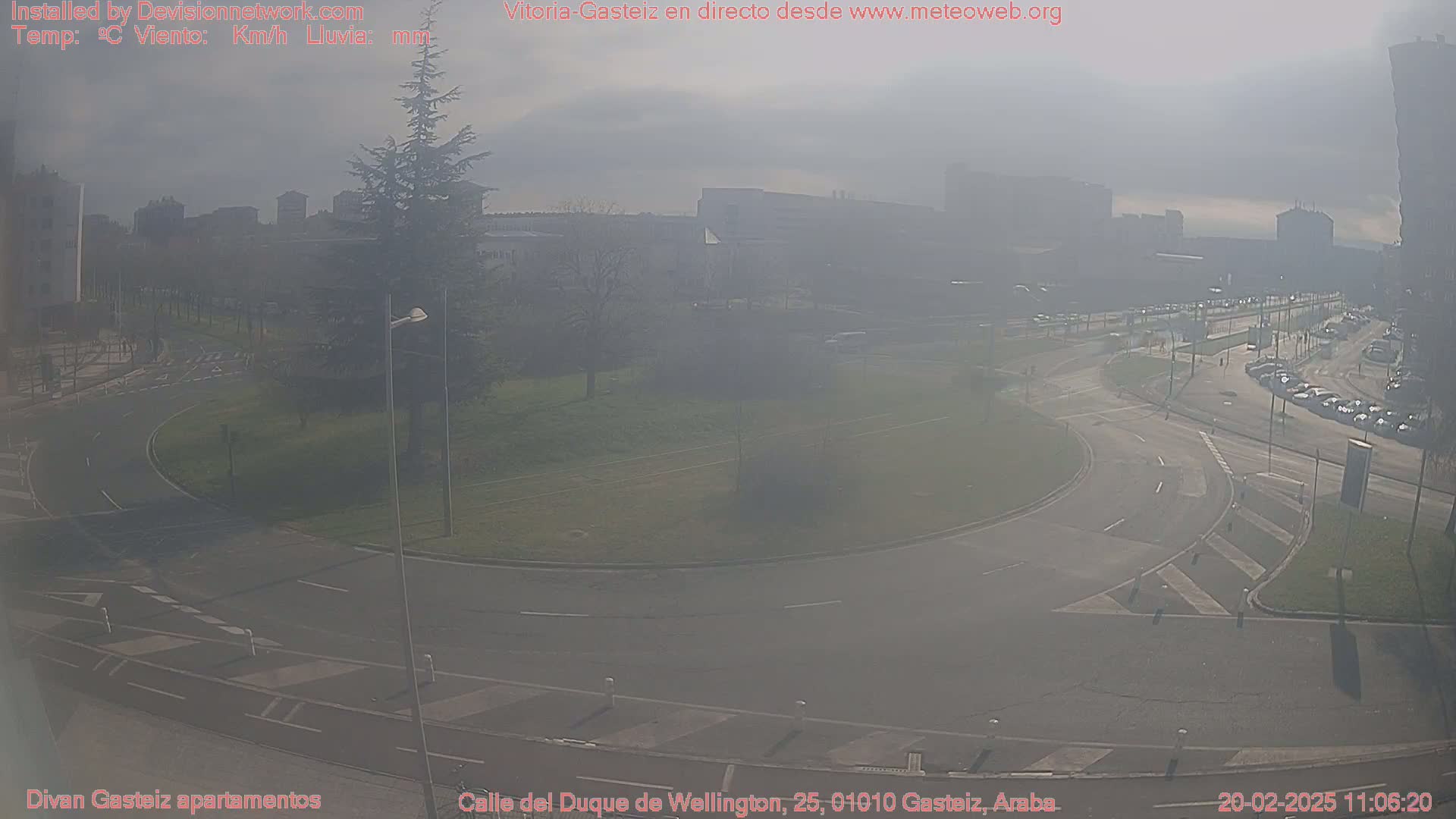 A hazy, sunny day reveals a roundabout and roads surrounded by buildings and trees in a city.