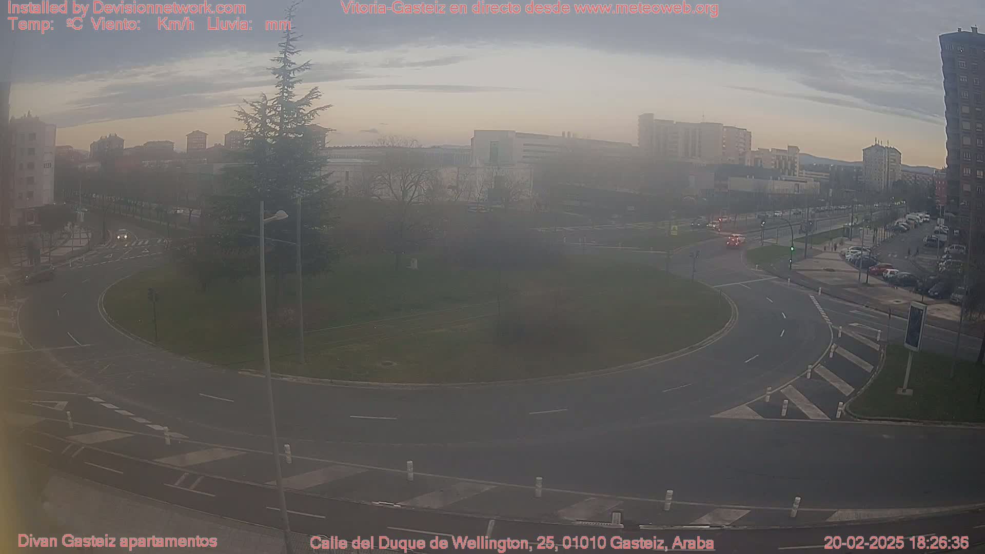 A hazy view of a roundabout and surrounding city streets, with several cars visible, under a dusky sky.