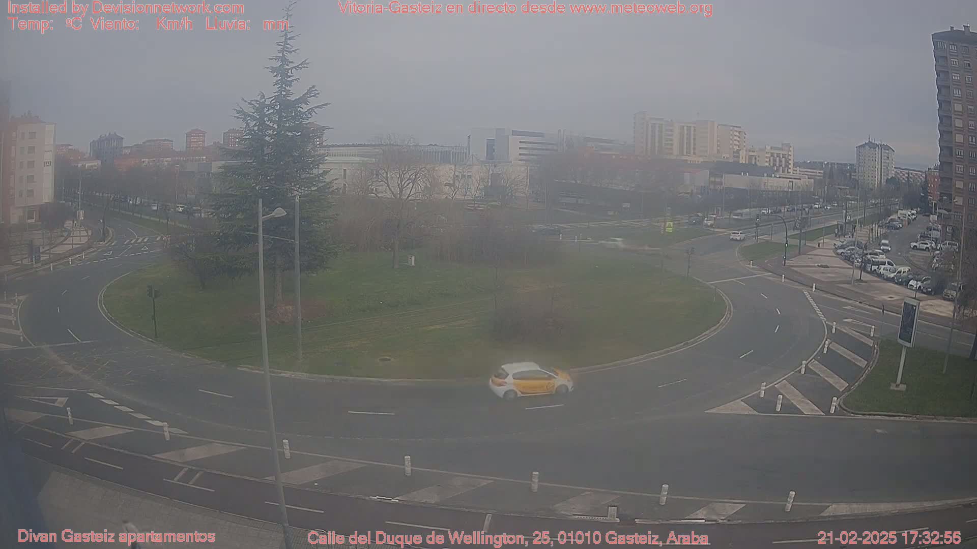 A hazy view of a roundabout and city streets with a few cars, under an overcast sky.