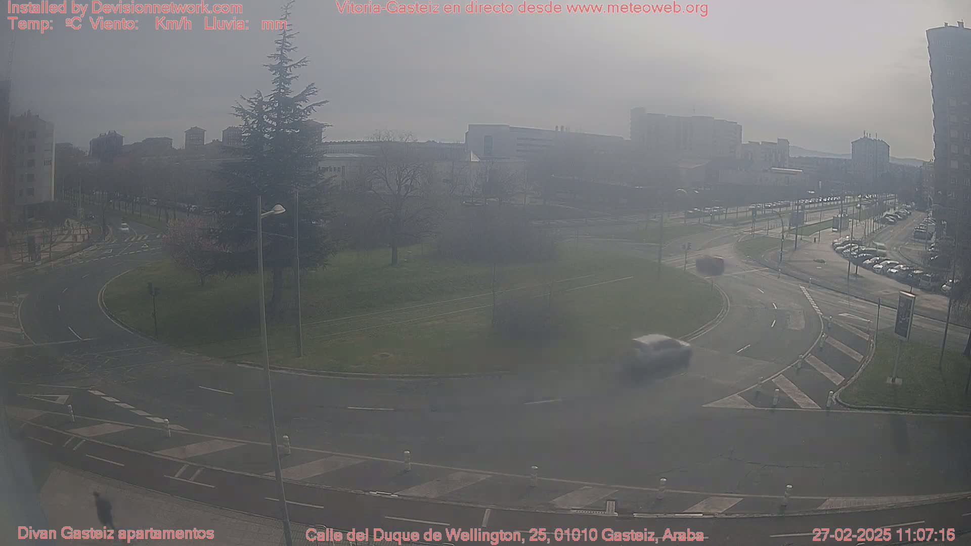 A hazy view of a roundabout and surrounding city streets, with several cars visible and buildings in the background.