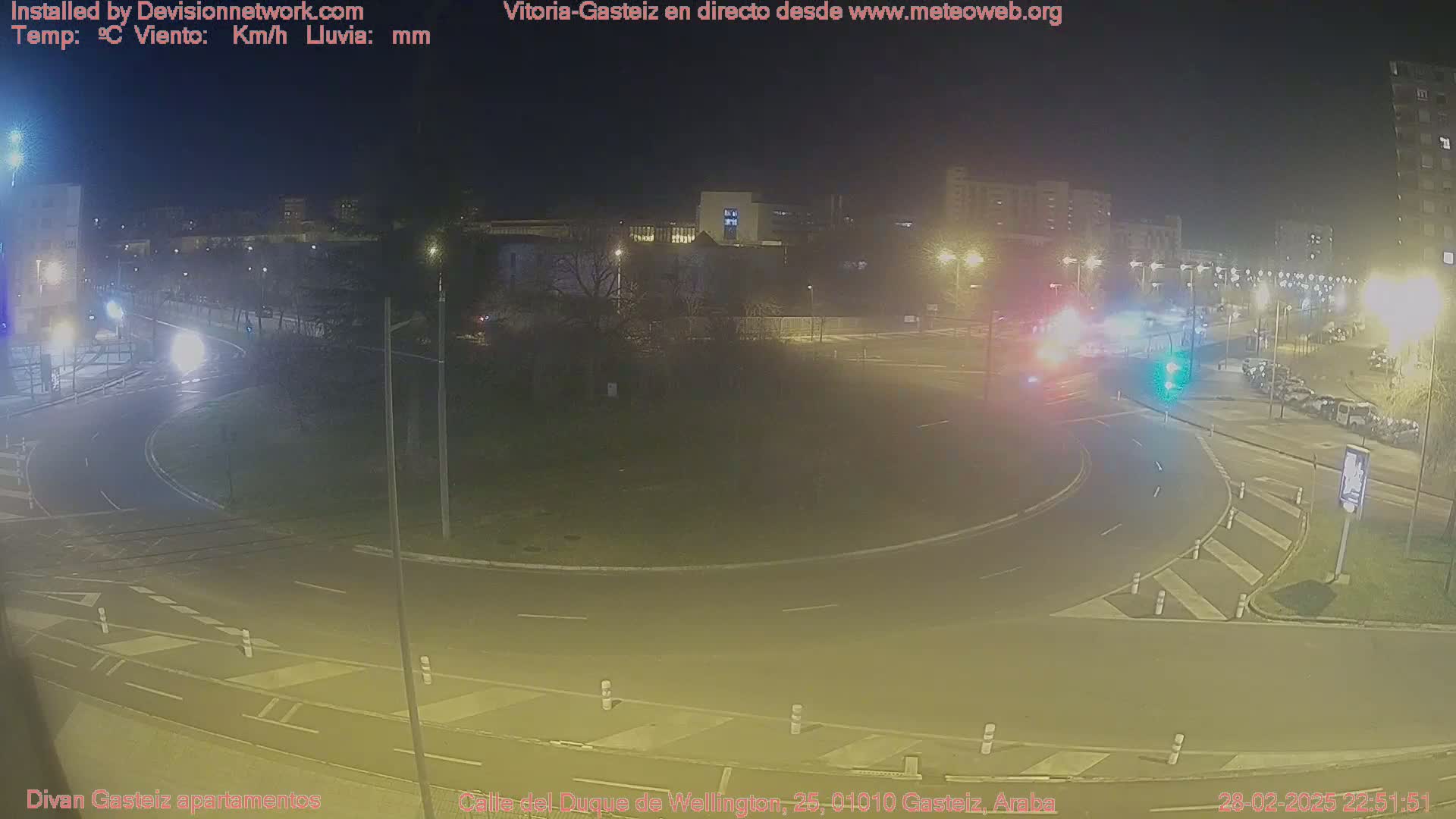 A nighttime view of a roundabout with several cars and streetlights, under clear skies.