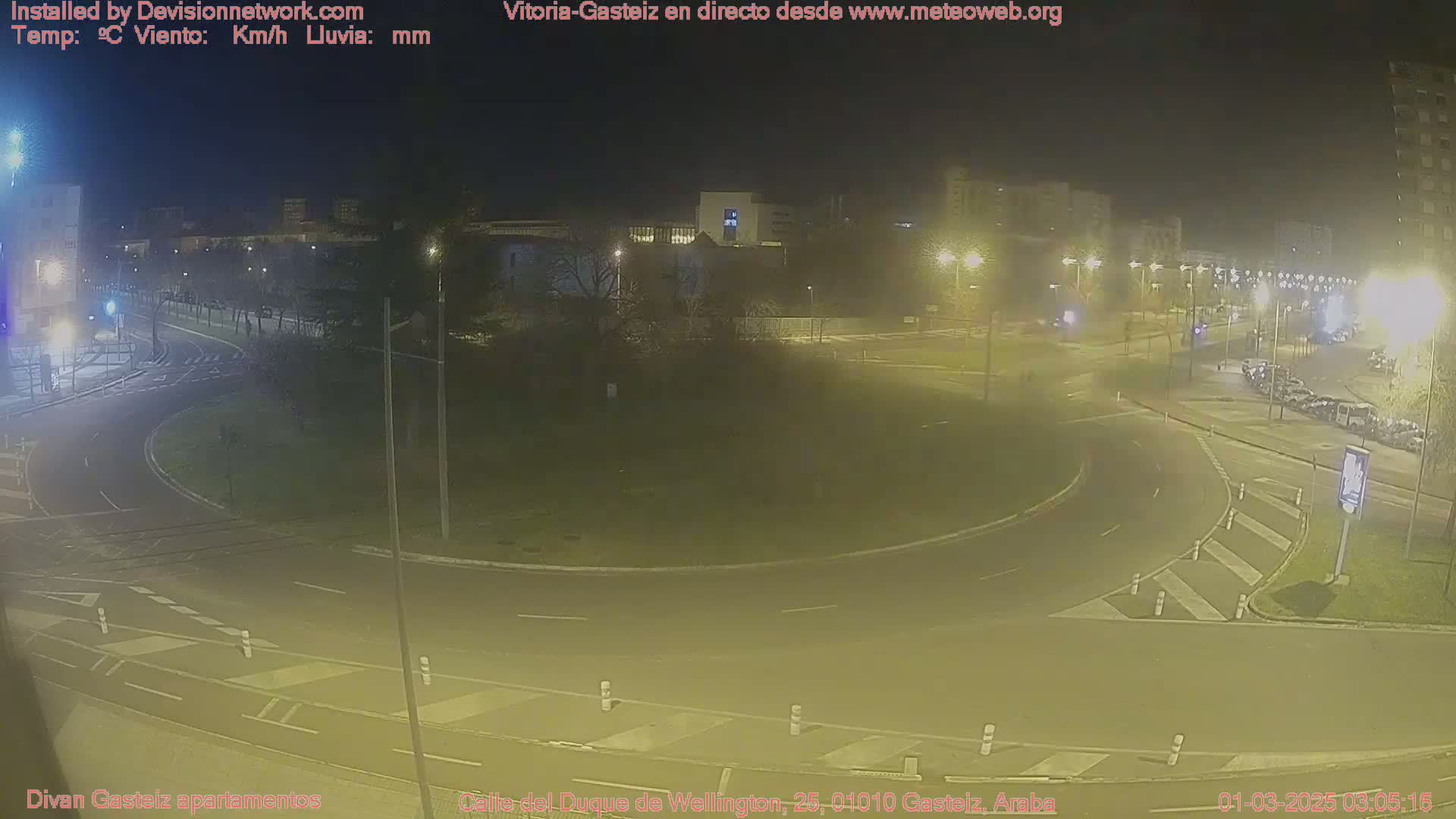 A nighttime view of a roundabout with minimal traffic, under hazy, dimly lit conditions.