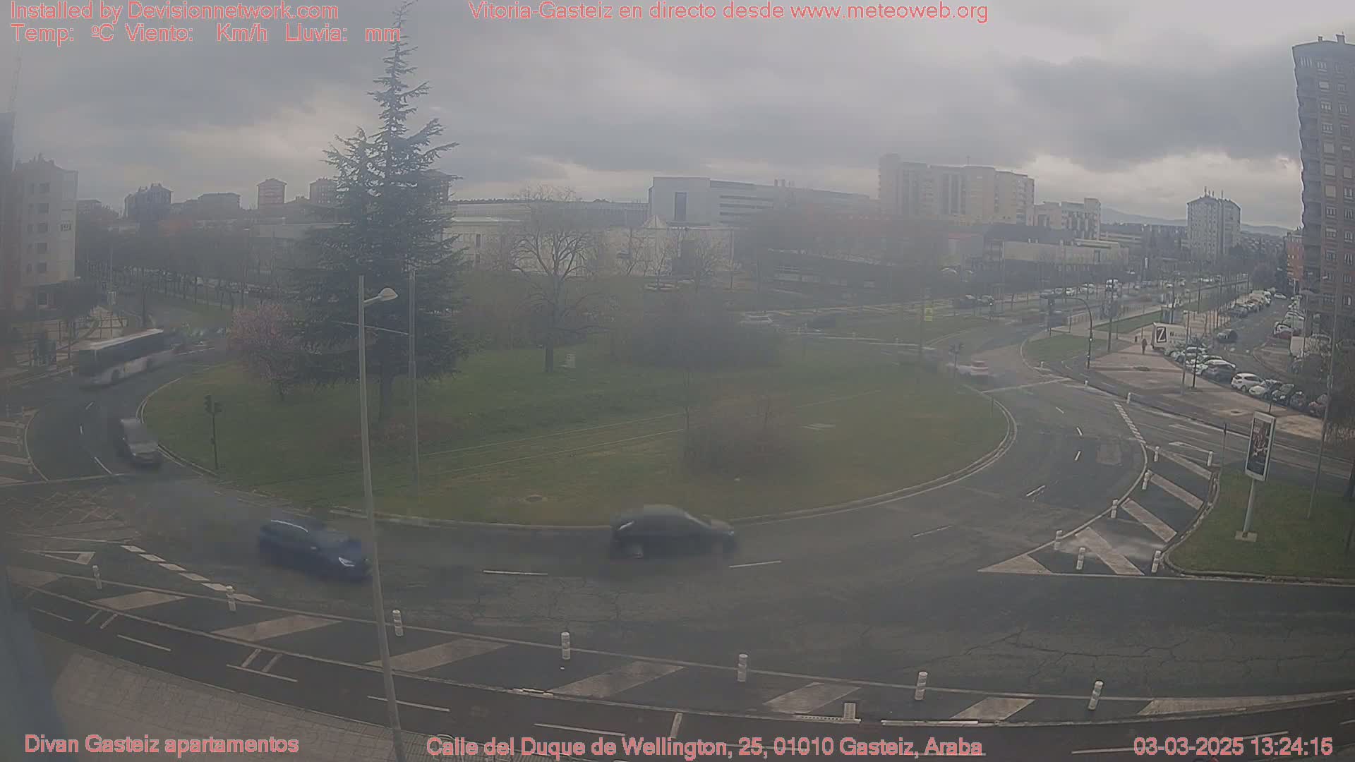 A hazy overcast day reveals a traffic circle surrounded by buildings and sparsely populated by vehicles, within a city.