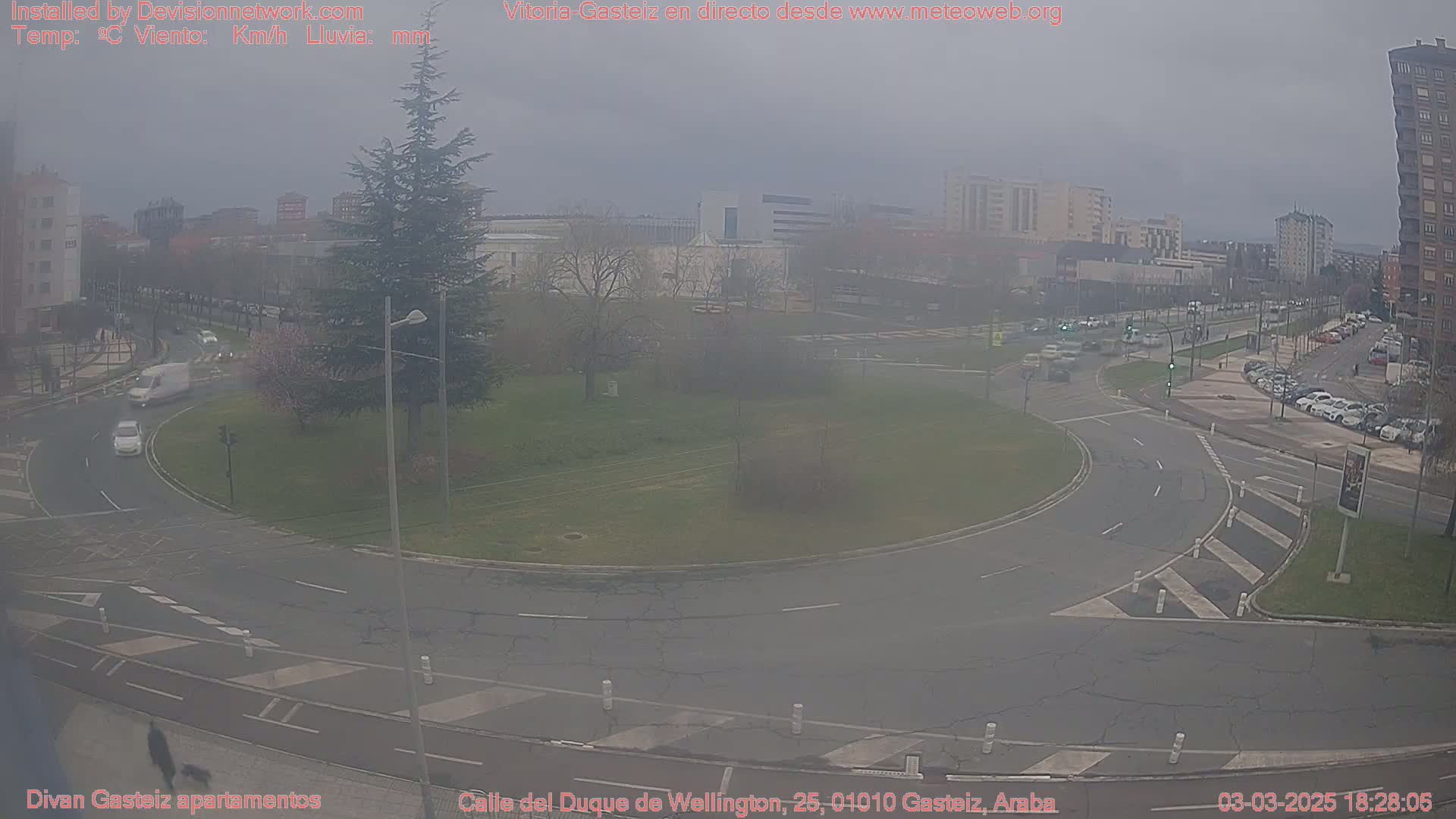 A hazy view of a roundabout and surrounding streets in a city, with several cars visible.