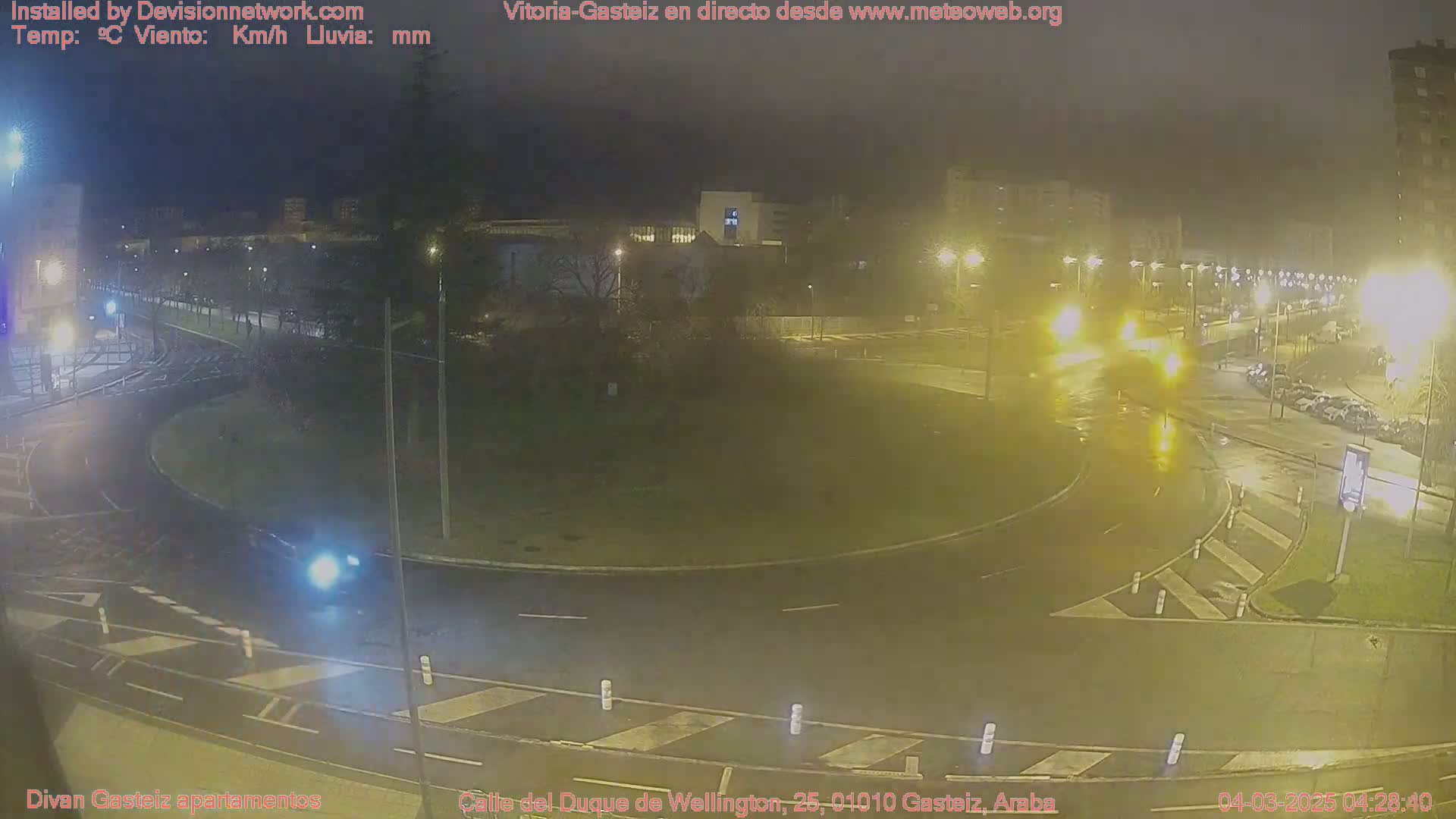 A wet, nighttime view of a roundabout with cars and streetlights in a city.