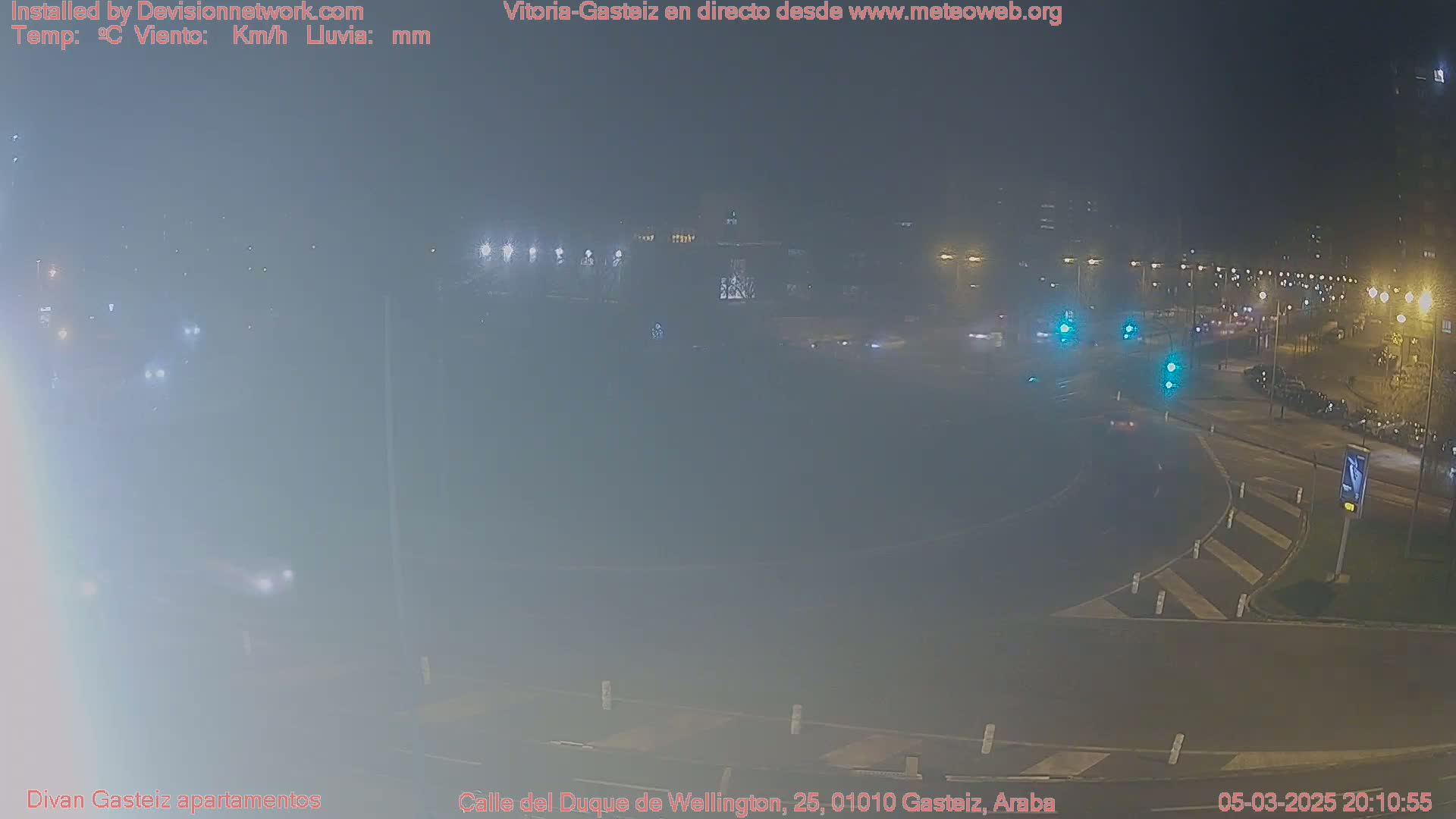 A hazy, nighttime view of a roundabout intersection with sparse traffic and streetlights.