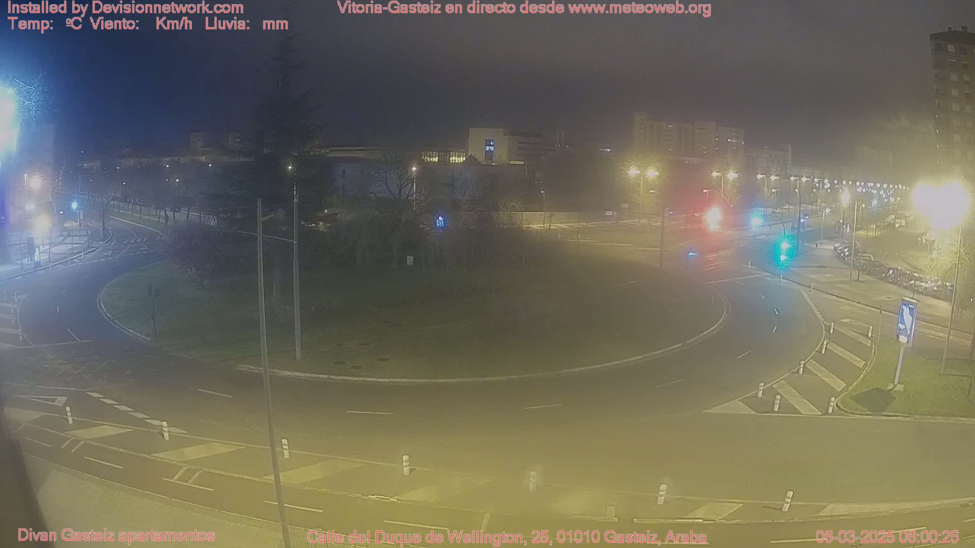 A nighttime view of a roundabout intersection with minimal traffic, under hazy or cloudy conditions.