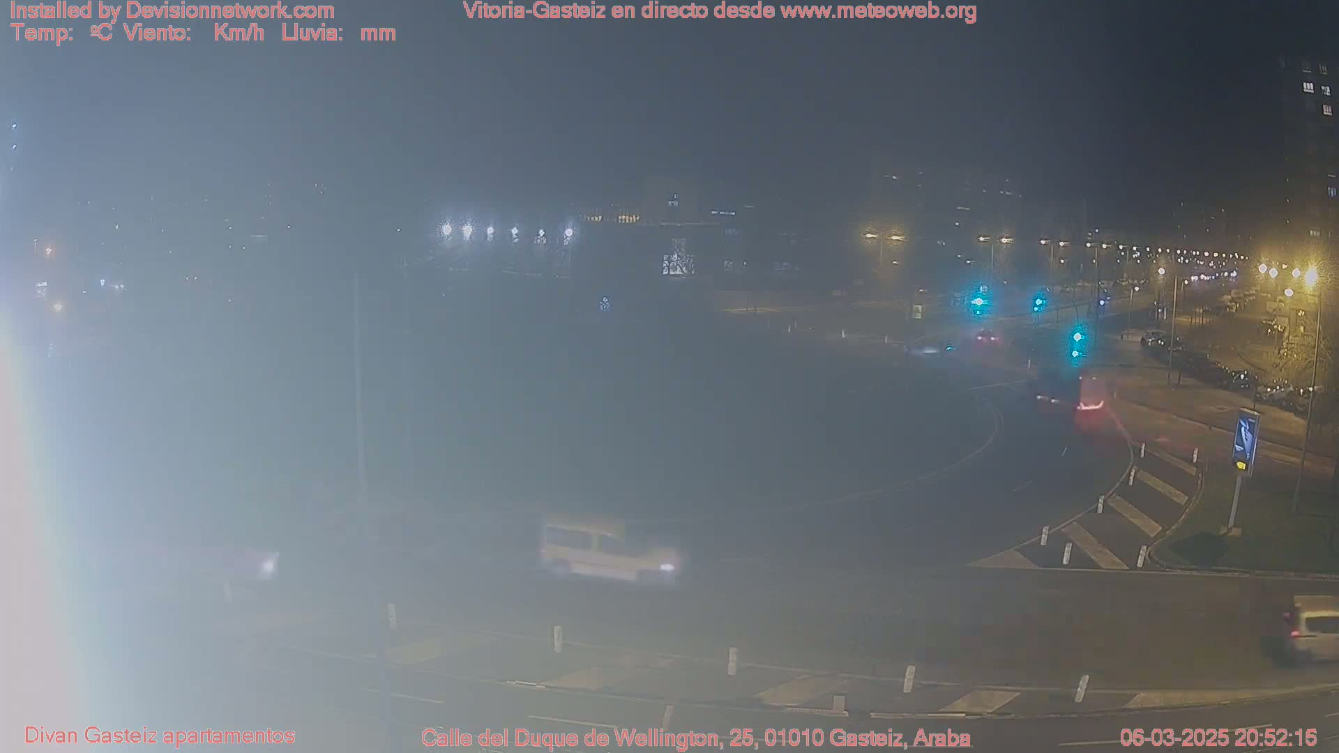 A nighttime, foggy view of a roundabout with several vehicles and streetlights.