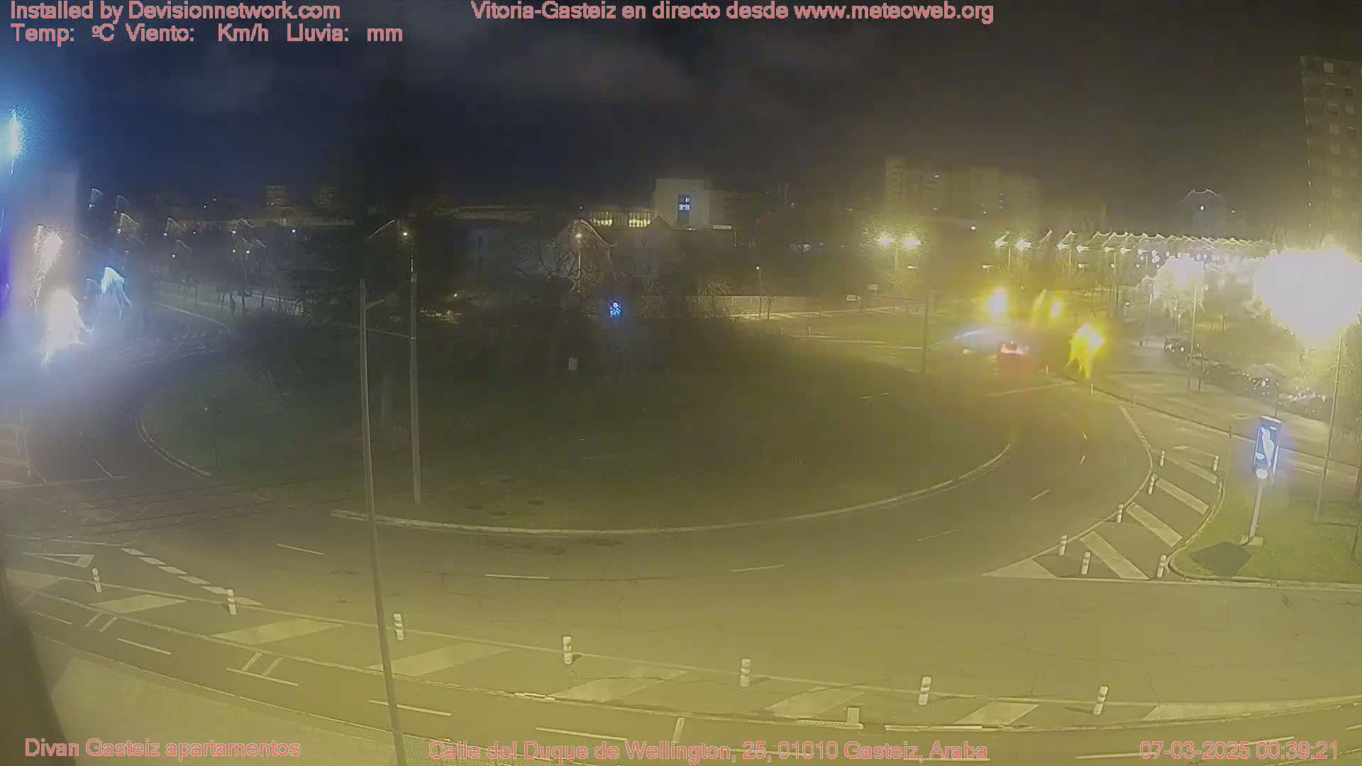 A nighttime view of a roundabout with minimal traffic, under partly cloudy skies.