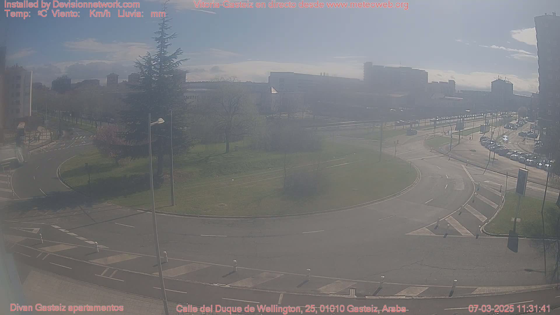 A hazy, sunny day overlooking a roundabout and city streets with parked cars and buildings in the distance.