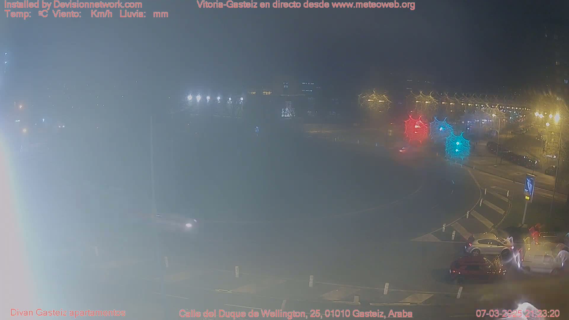 A foggy night scene shows a roundabout with several cars and streetlights.