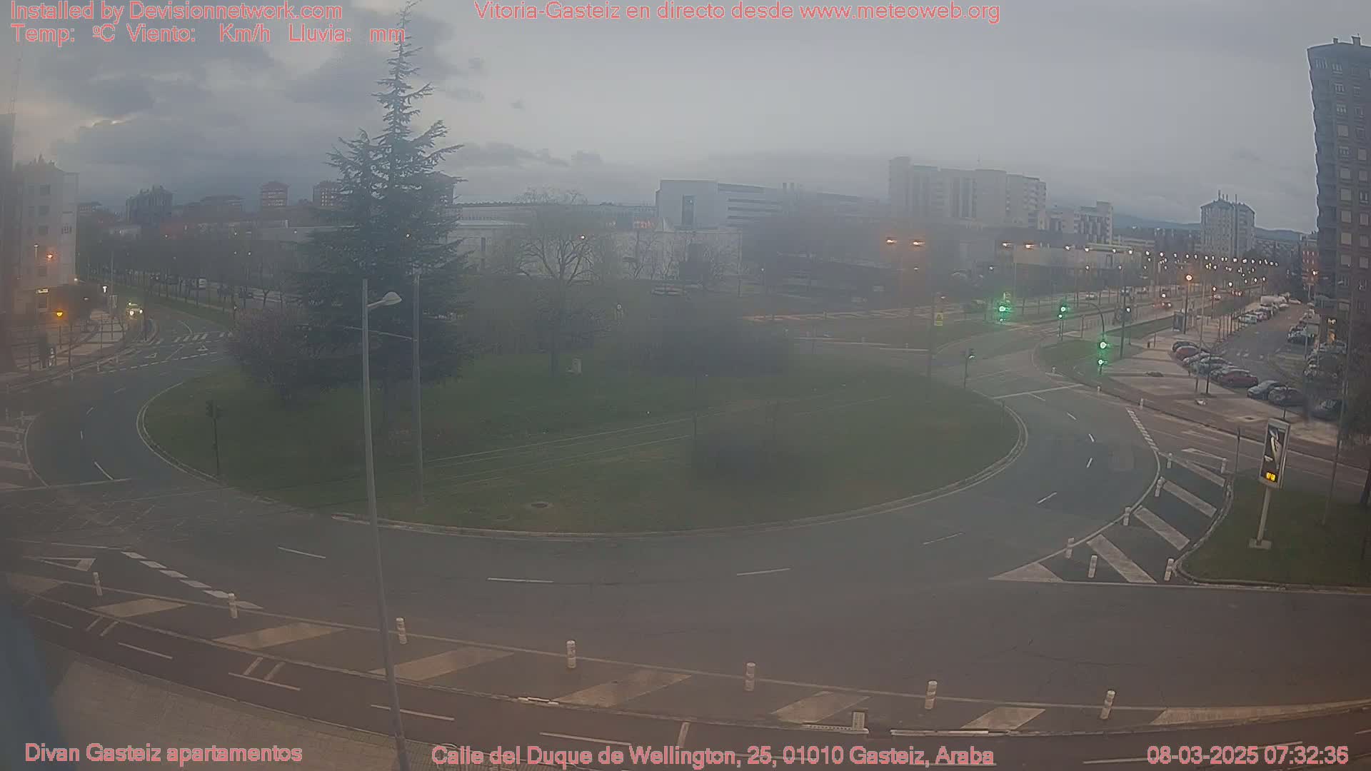 A hazy, overcast day reveals a roundabout surrounded by buildings and parked cars in a city setting.