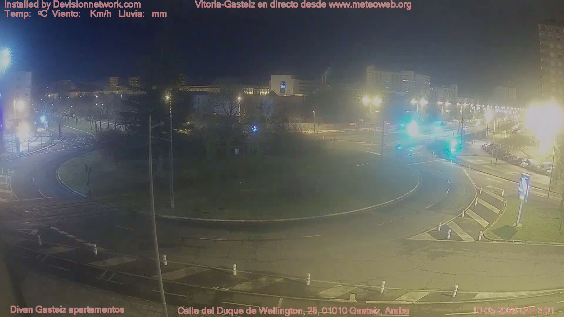 A nighttime view of a roundabout and surrounding streets, with several vehicles and streetlights visible under a dark, clear sky.