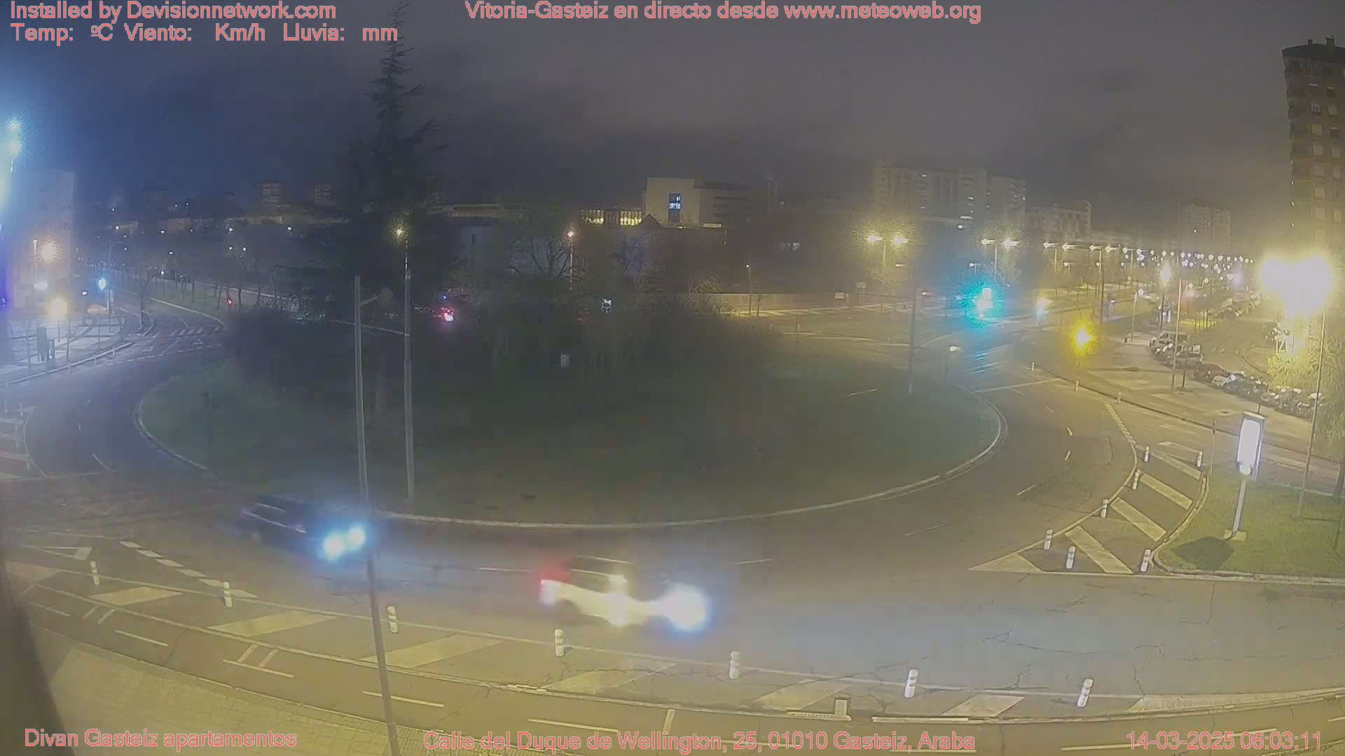 A nighttime view of a roundabout with several cars and streetlights, under hazy or overcast conditions.