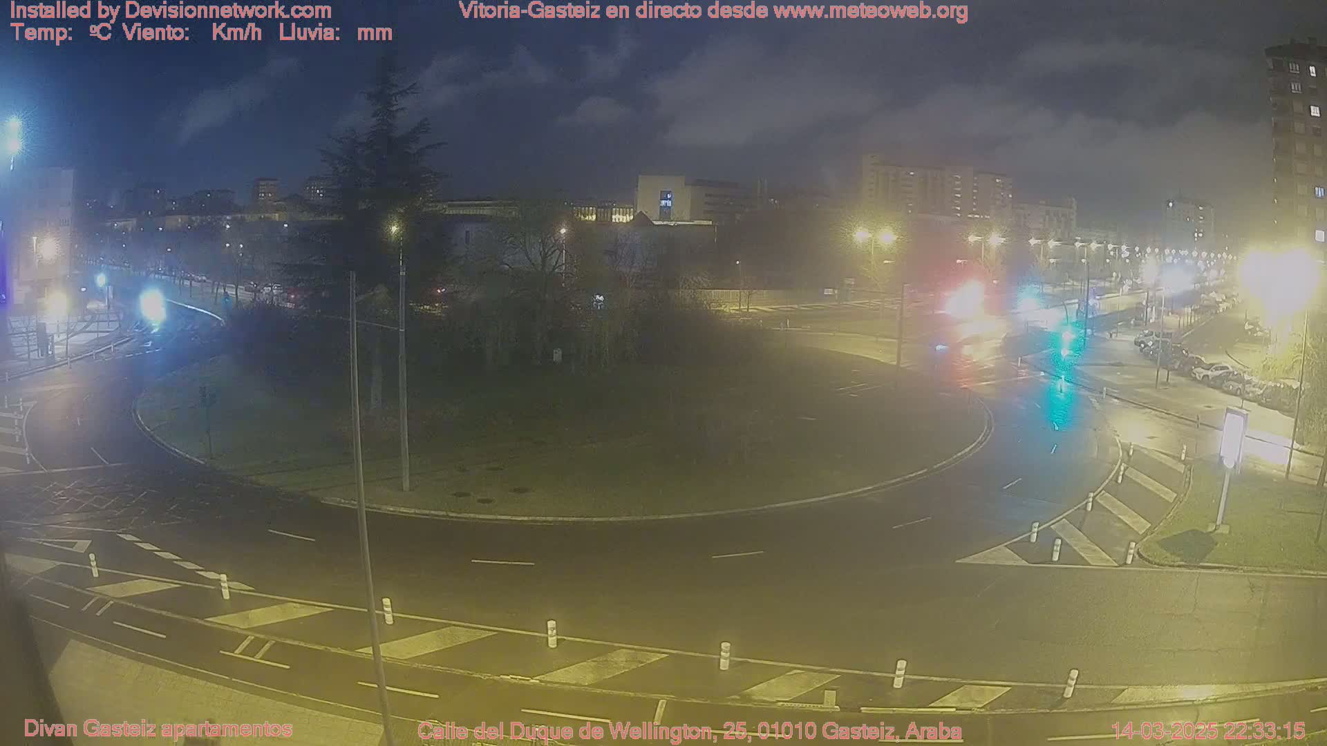A nighttime view of a roundabout with cars and streetlights, under a cloudy sky.