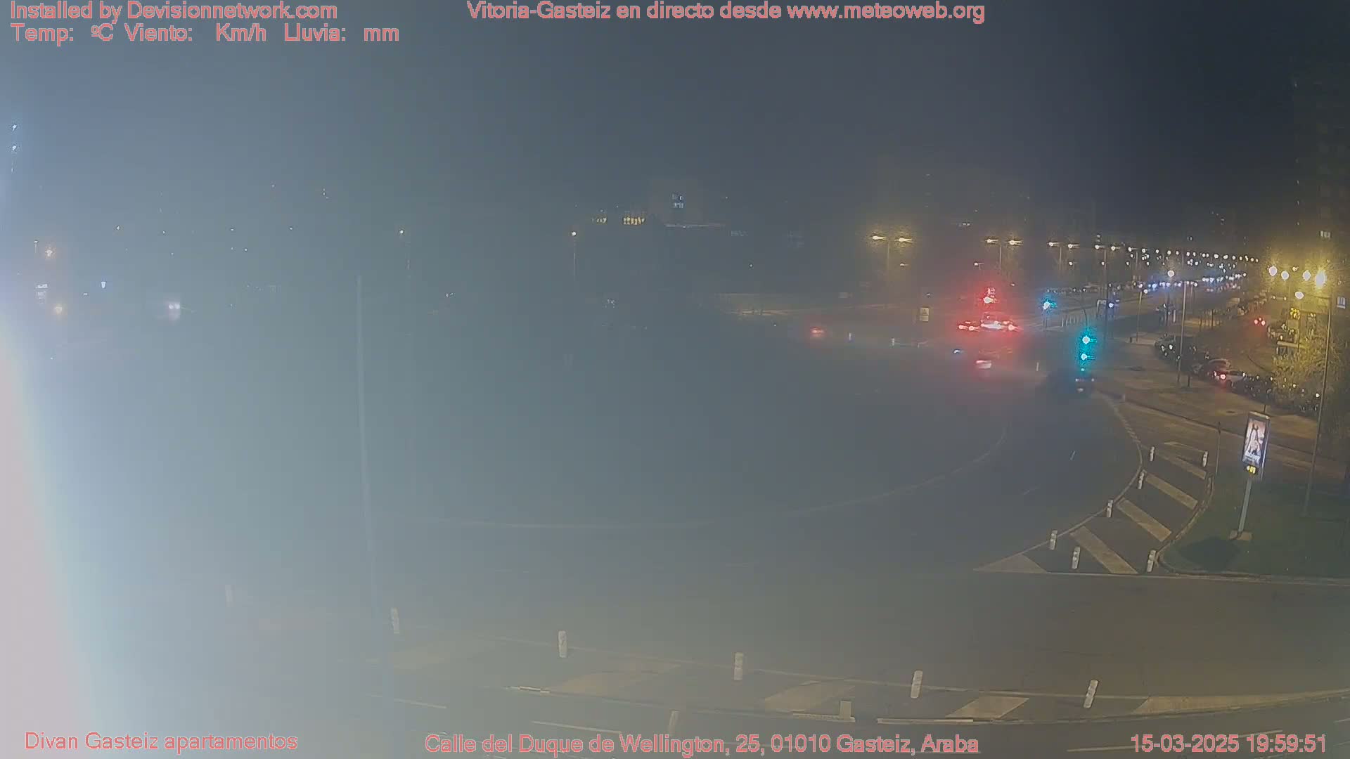 A hazy night scene shows a street intersection with several vehicles and streetlights under a foggy sky.