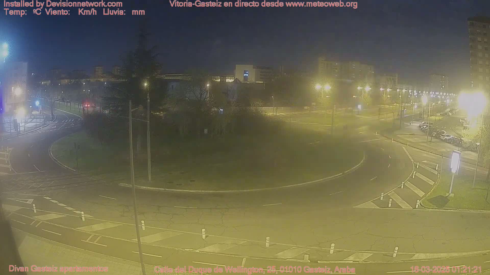 A nighttime view of a roundabout and surrounding streets, illuminated by streetlights under hazy conditions.