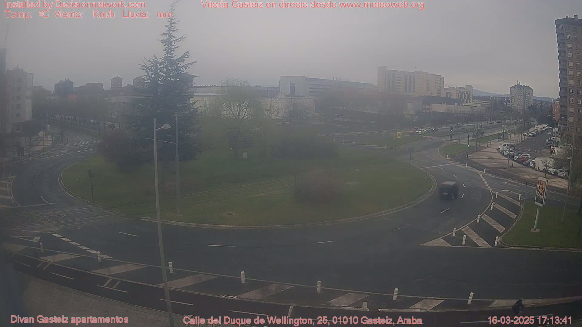 A hazy, overcast view of a roundabout and surrounding city streets, with several cars visible.