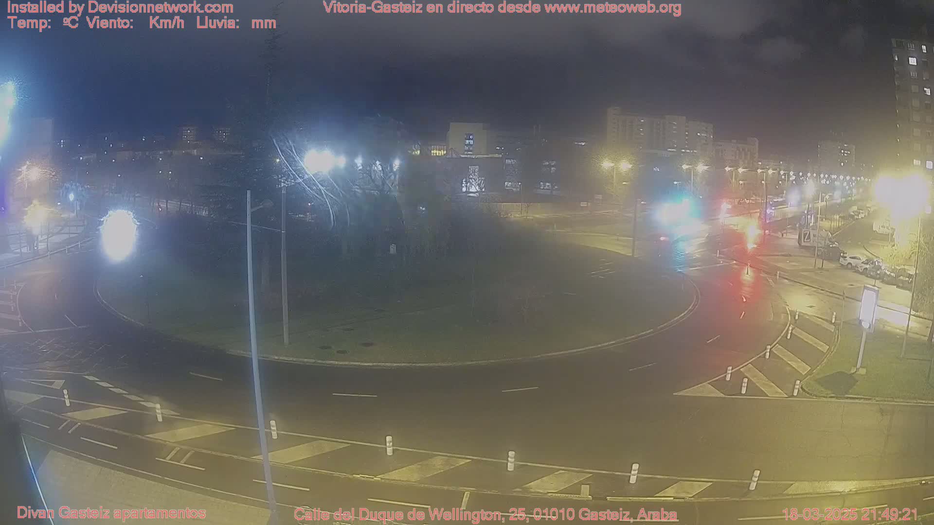 A nighttime view of a traffic circle with cars and streetlights, under cloudy conditions.