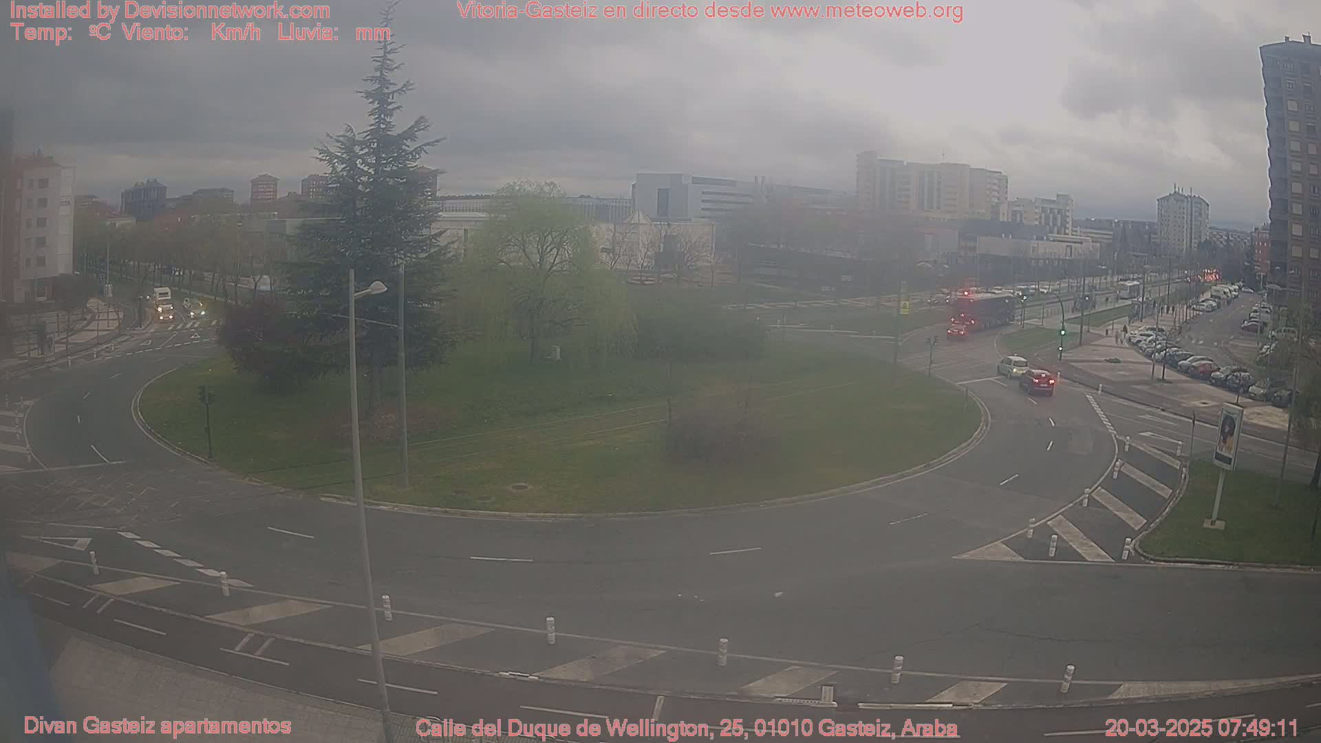 A hazy, overcast day reveals a roundabout in a city with several vehicles and buildings visible in the distance.