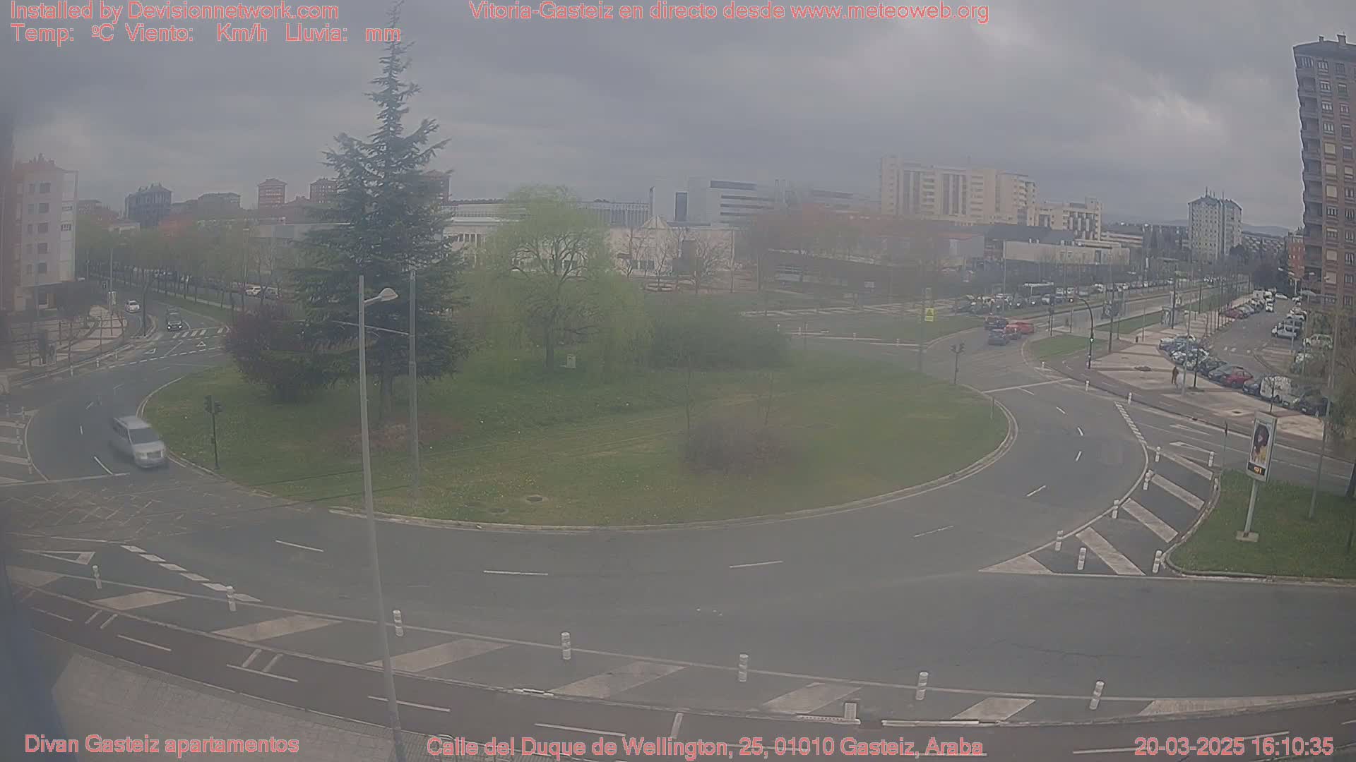 A hazy view of a roundabout and surrounding city streets with several cars visible, under an overcast sky.