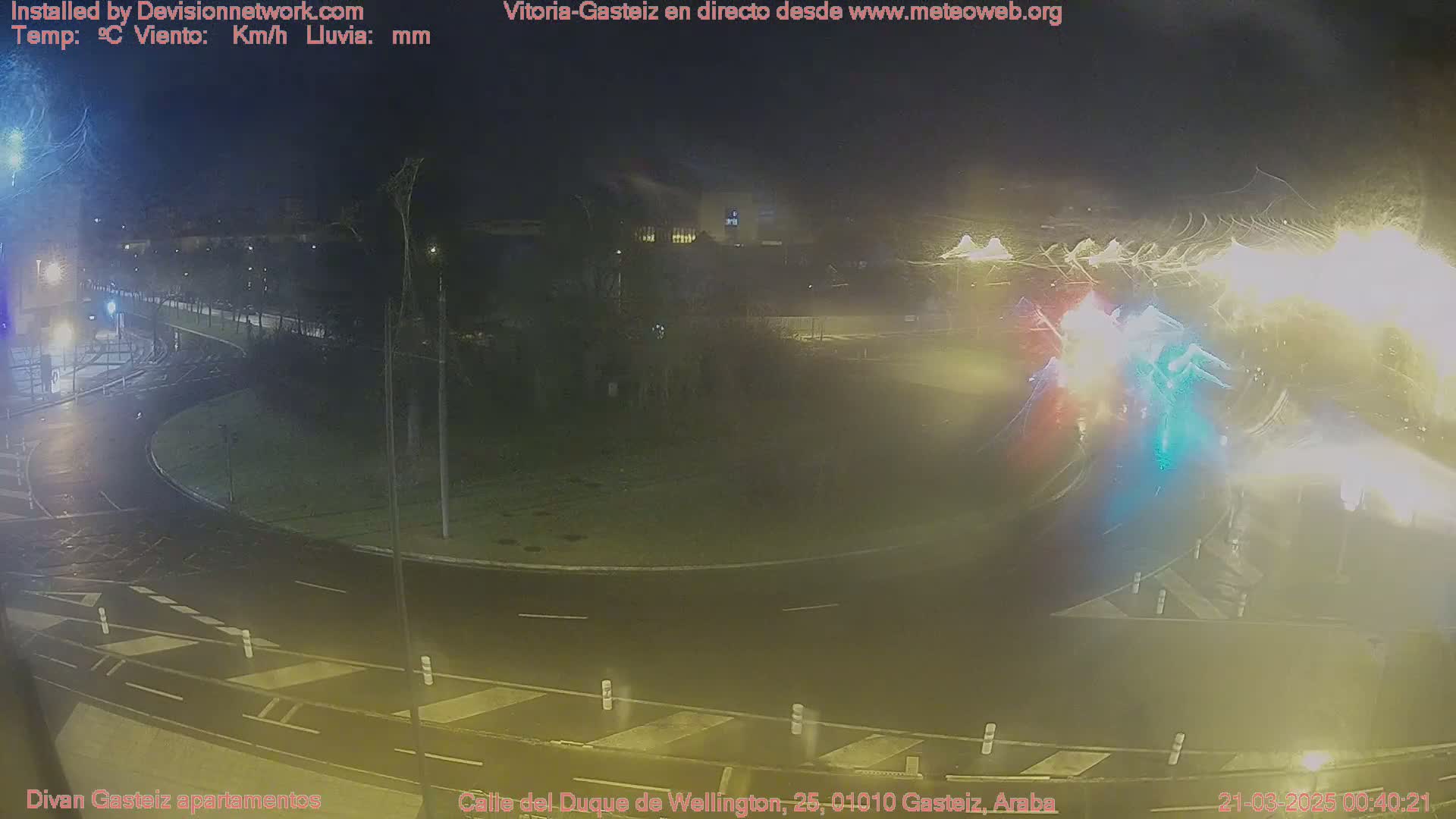 A nighttime view of a wet roundabout and surrounding roadways, illuminated by streetlights and vehicle headlights.