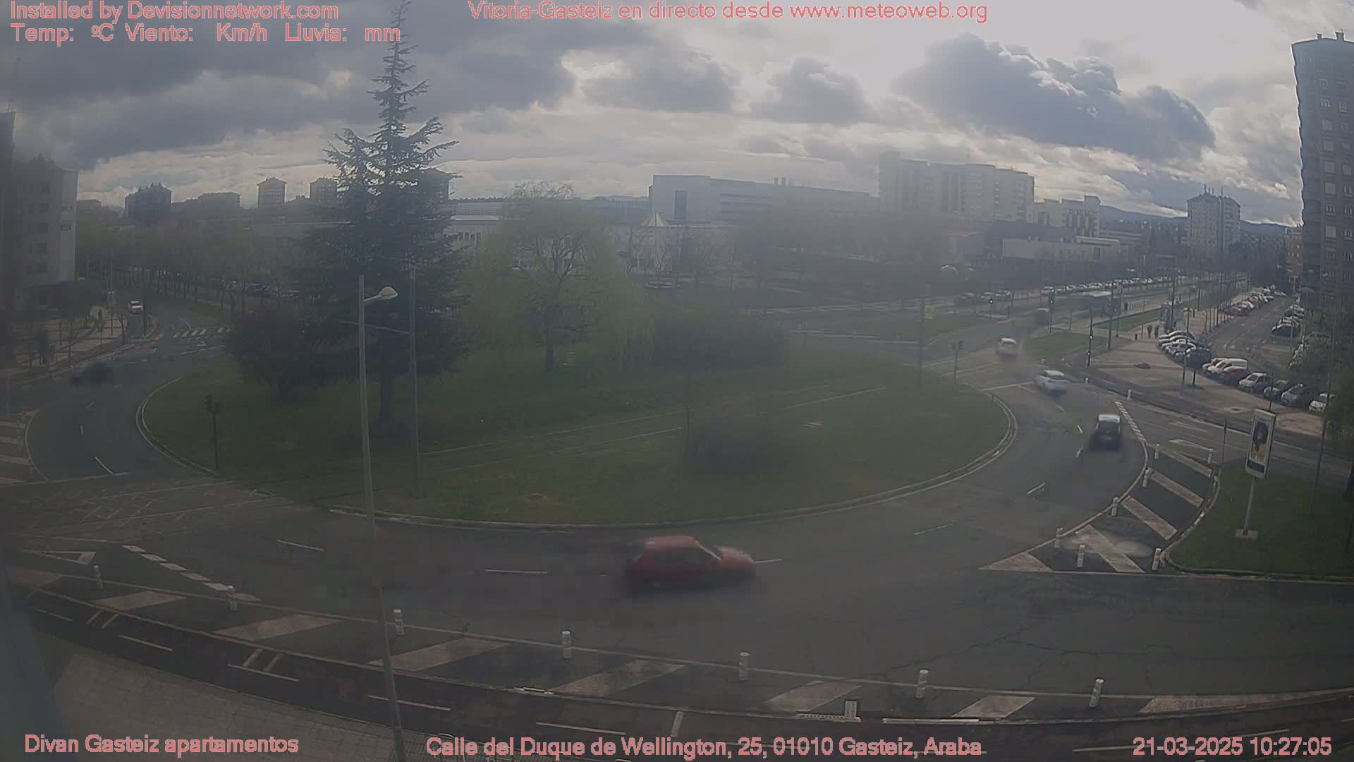 A hazy, overcast day shows a roundabout with several cars and a cityscape in the background.
