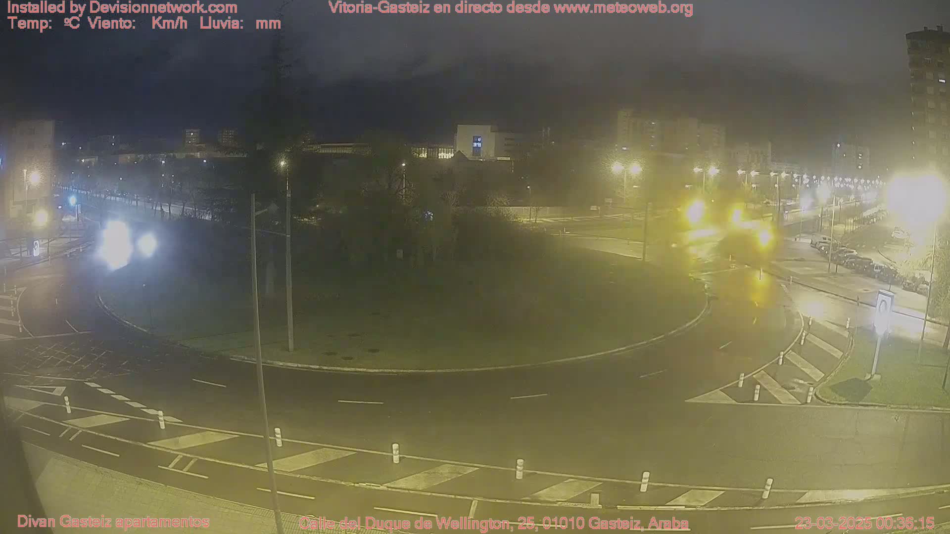 A nighttime, wet view of a roundabout with cars and streetlights in a city.