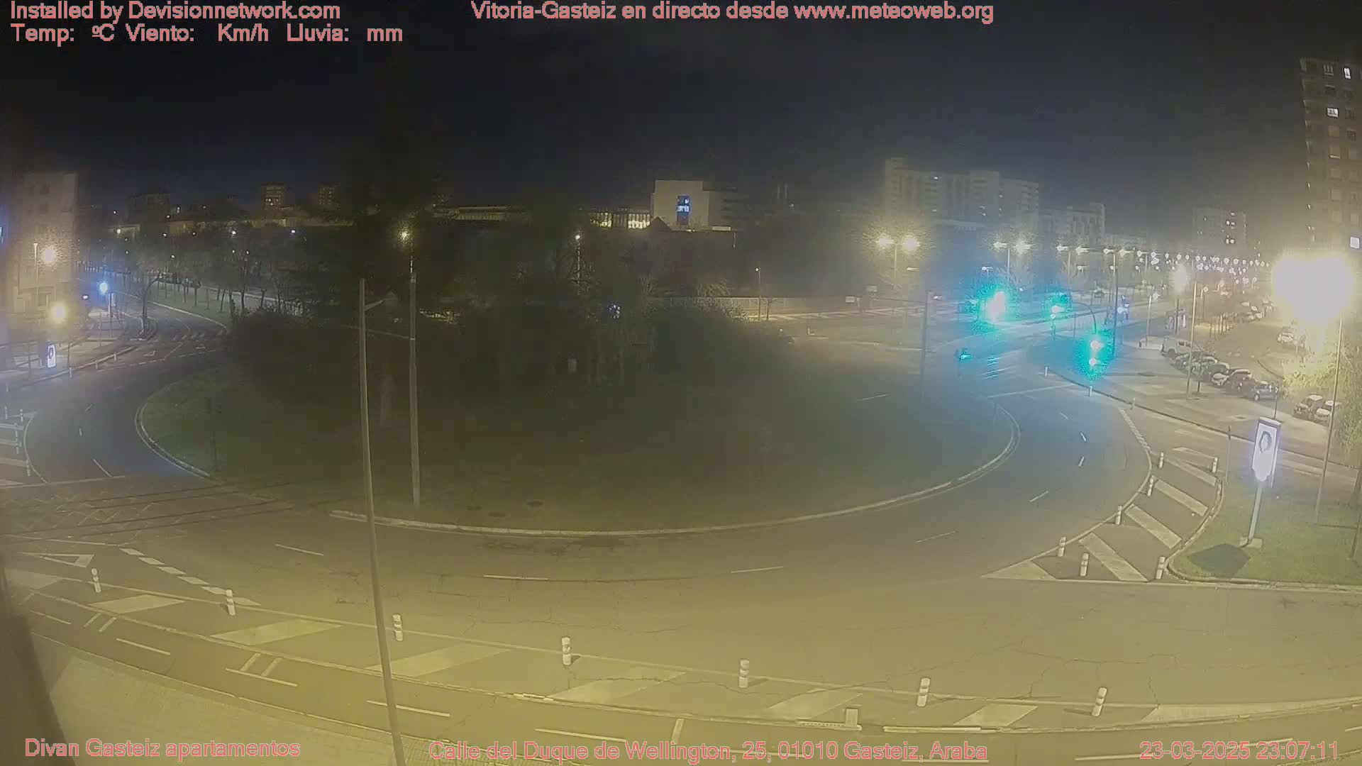A nighttime, high-angle view of a roundabout intersection with several vehicles and streetlights illuminating the scene.