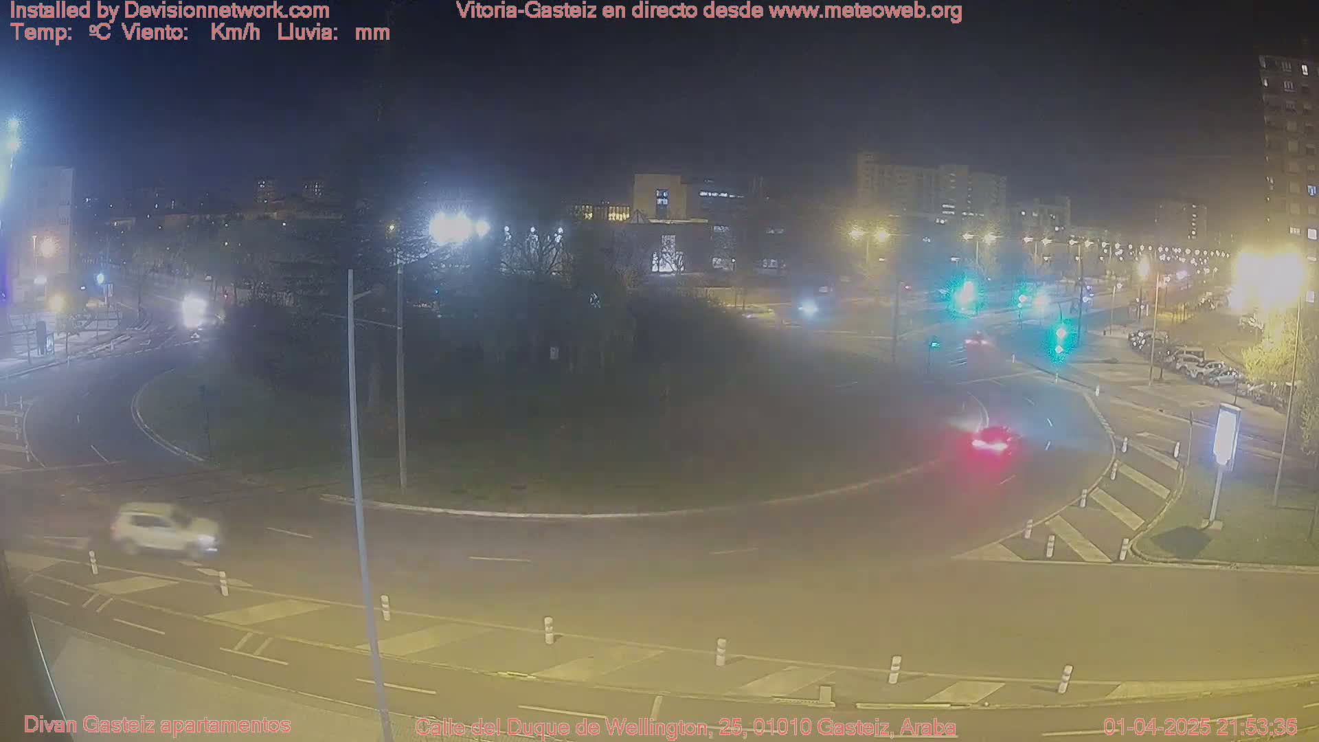 A nighttime view of a roundabout with several cars and streetlights, under clear skies.