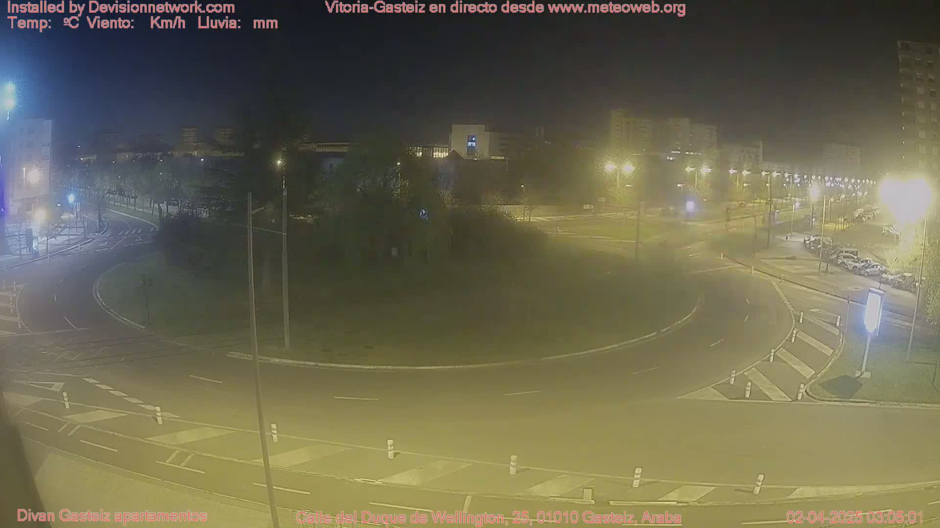 A nighttime view of a roundabout with cars and streetlights, under hazy conditions.