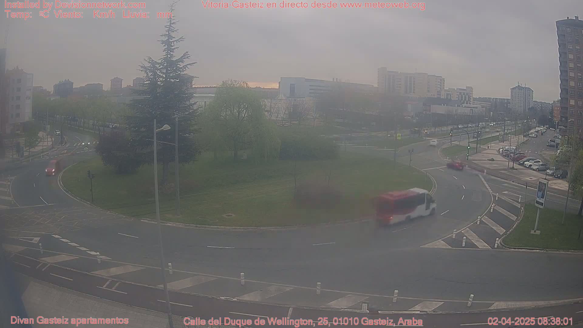 A hazy view of a roundabout in a city with several cars and a bus visible, under an overcast sky.