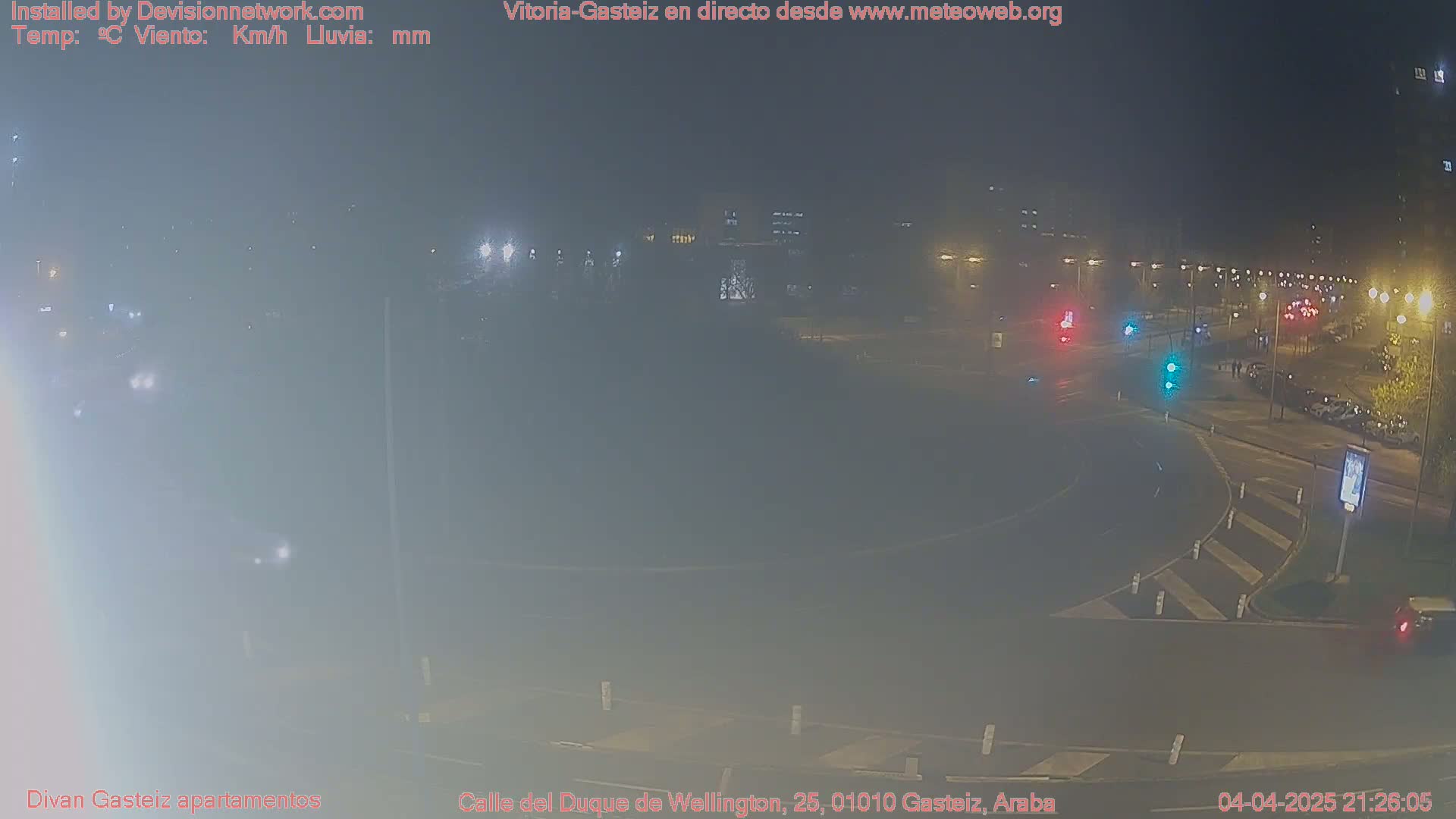 A hazy night scene shows a roundabout with cars and traffic lights, and buildings in the background.