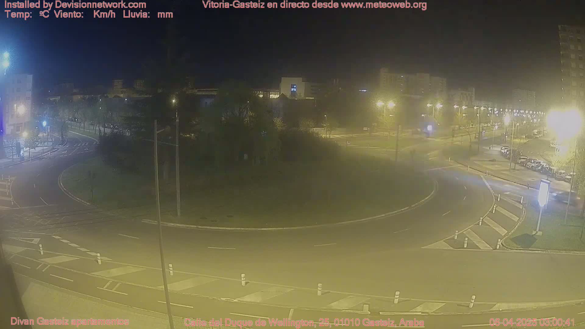 A nighttime view of a roundabout with minimal traffic, illuminated by streetlights under a clear, dark sky.